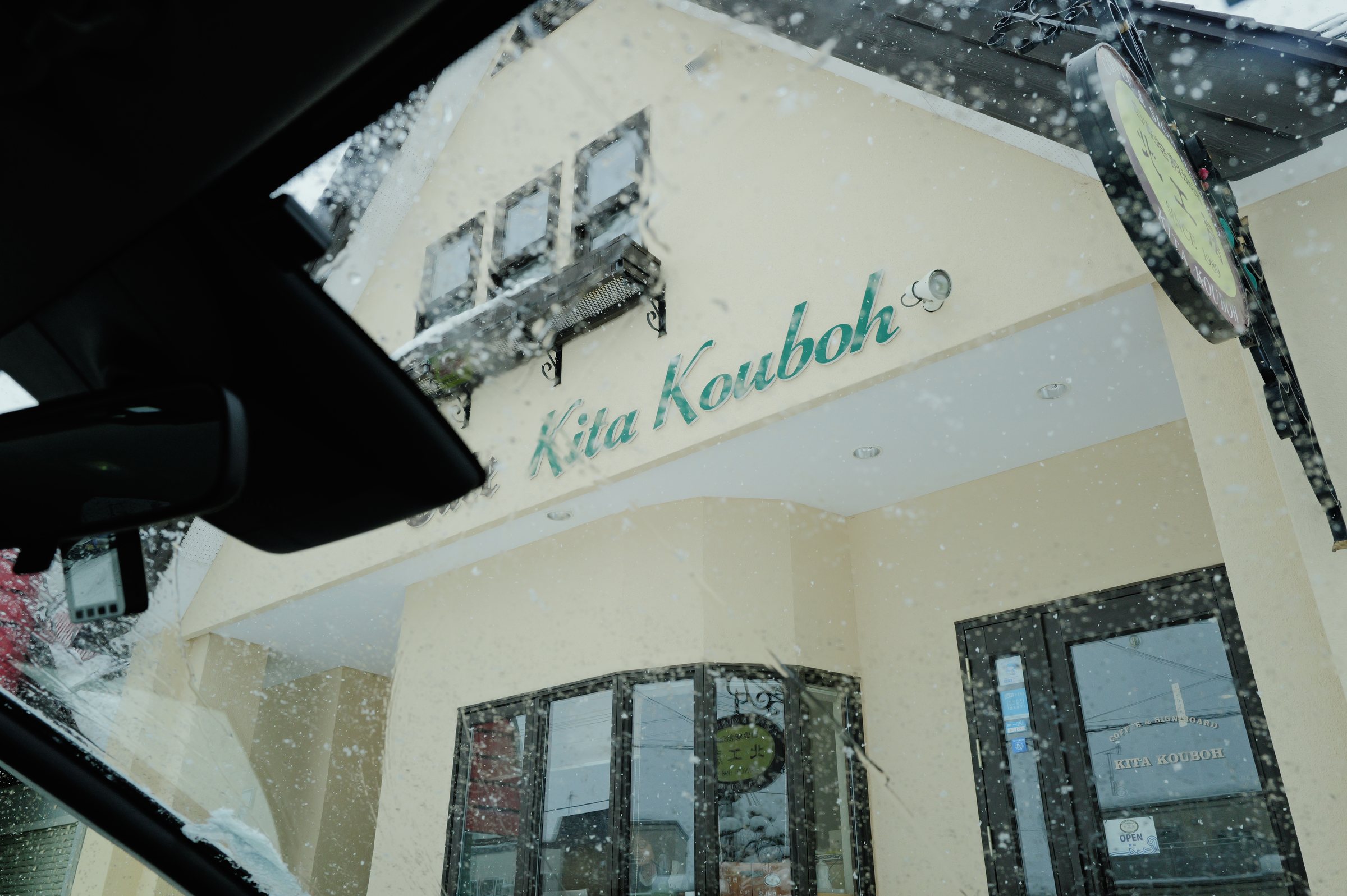 雪の降るフロントガラス越しに見える、珈琲店の建物