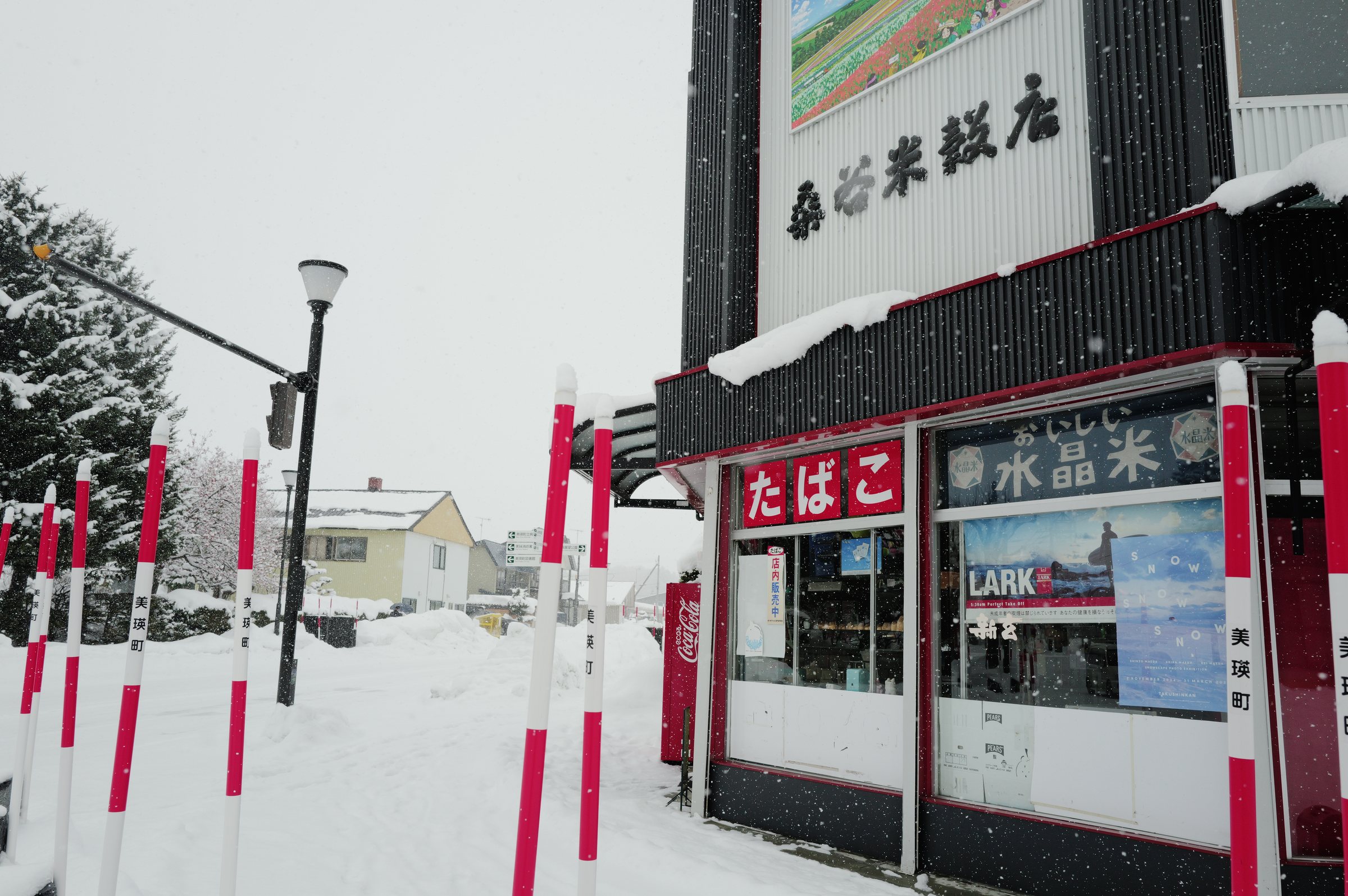 紅白のポールが並ぶ角に建つ、米屋の店先