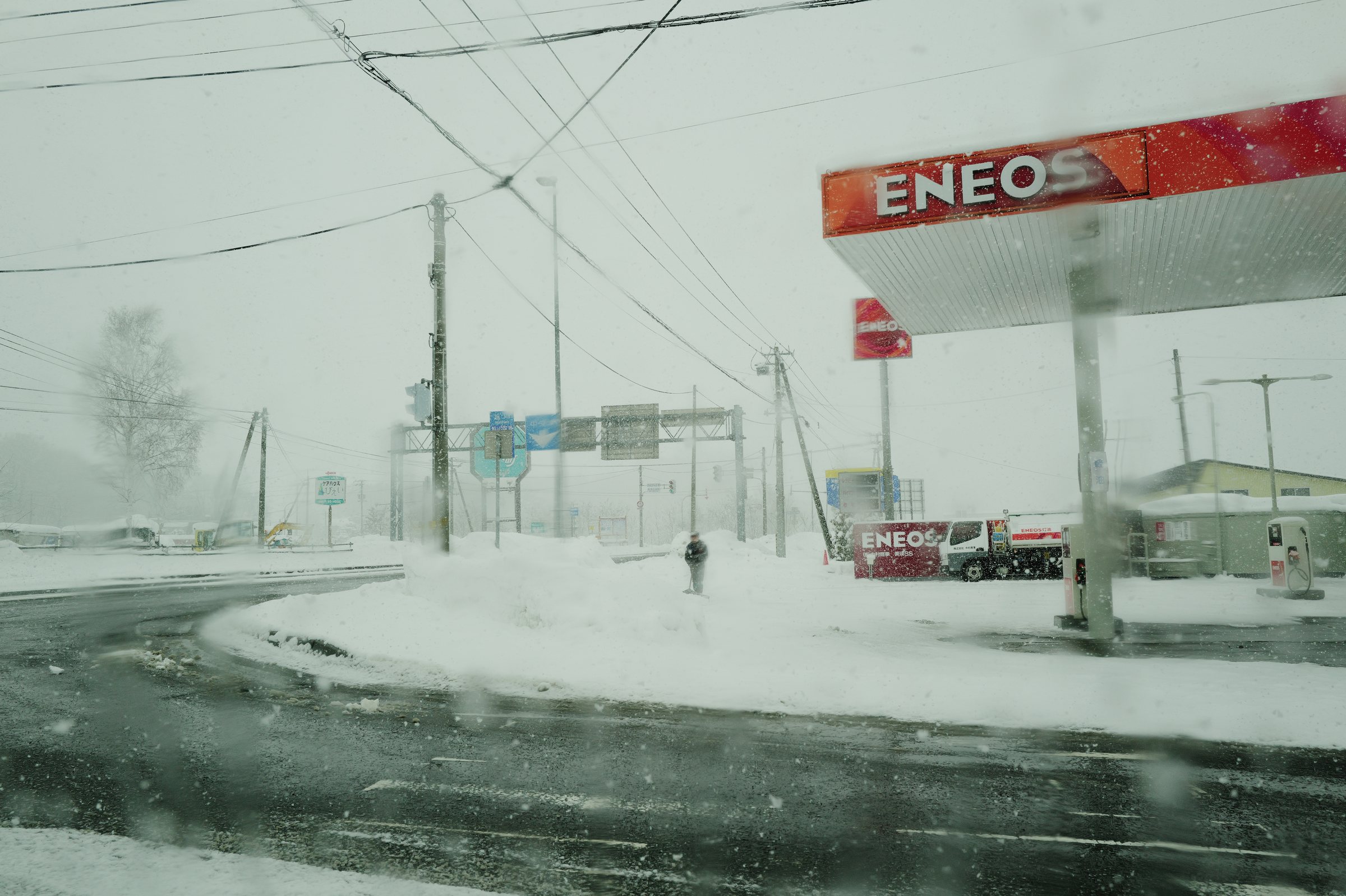 吹雪で白く霞むガソリンスタンドと交差点