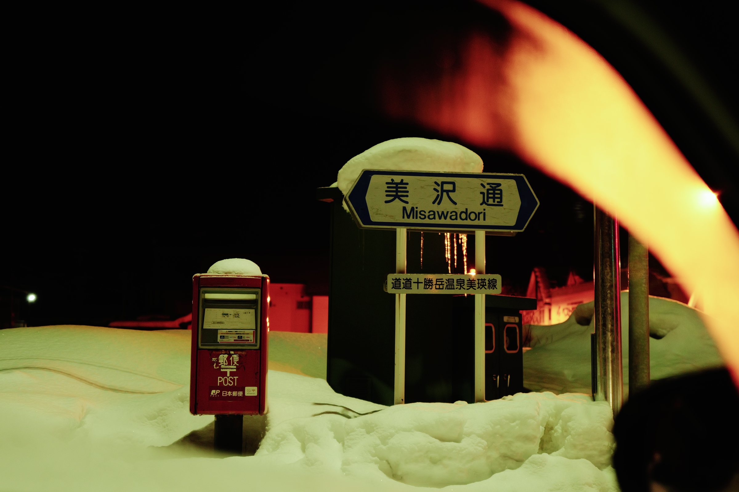 夜、雪をかぶった通りの名前の板と、雪に埋もれた赤いポスト