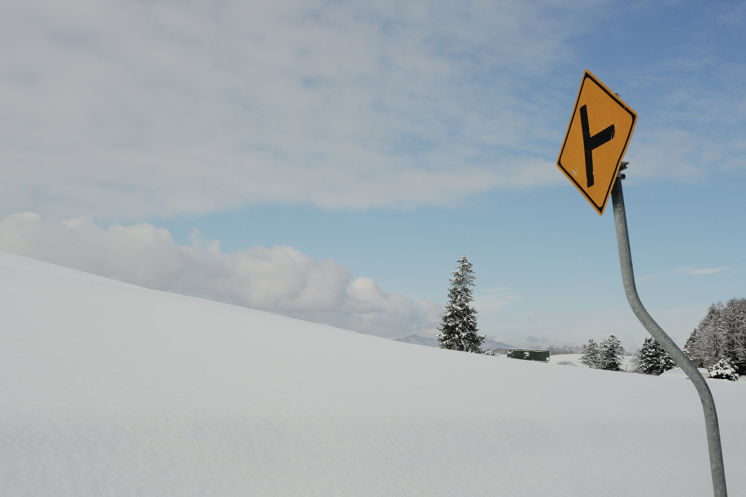 雪の丘の道端に立つ、分かれ道を知らせる黄色い標識
