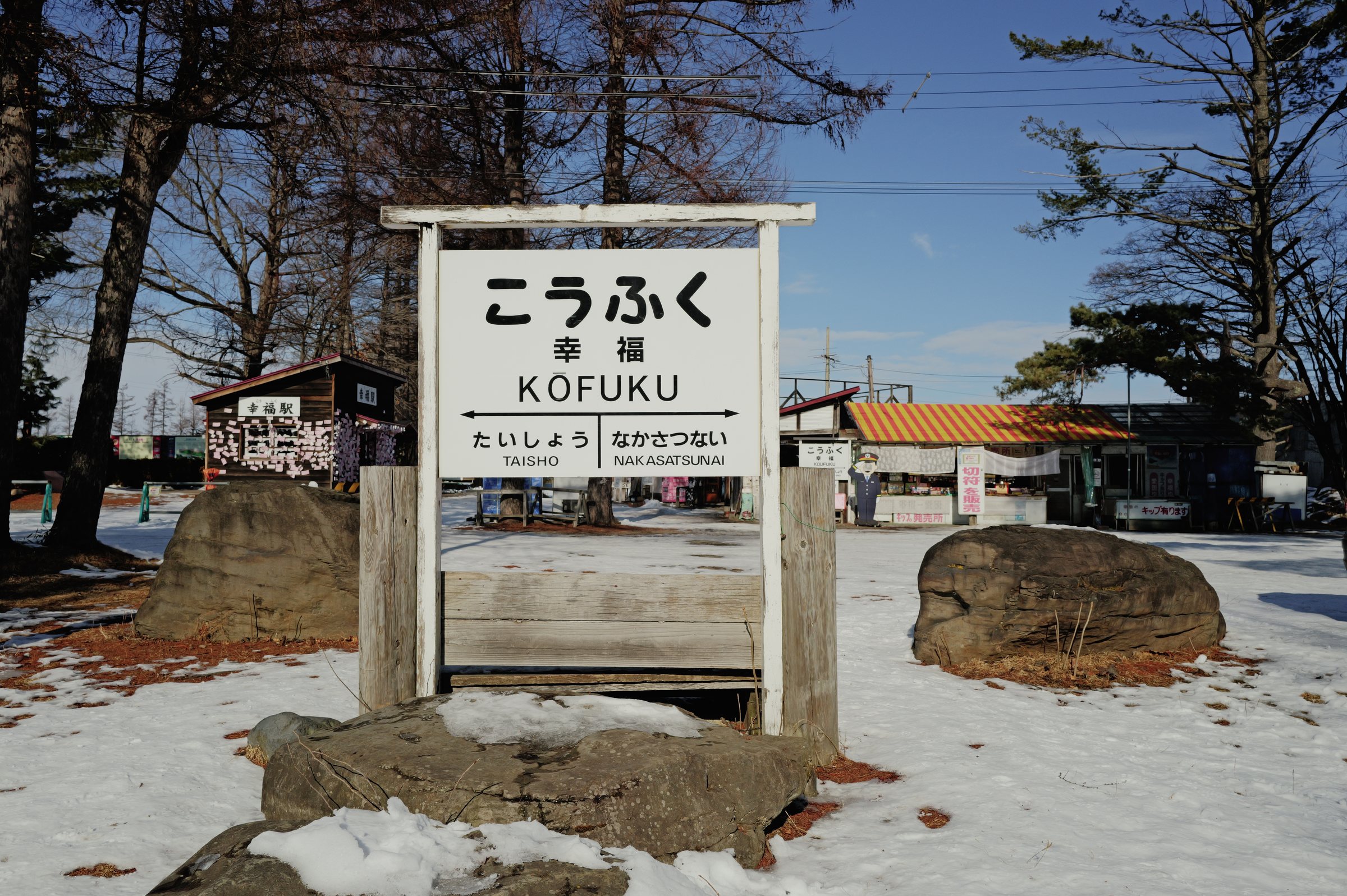 雪の残る地面に立つ「こうふく」の駅名標