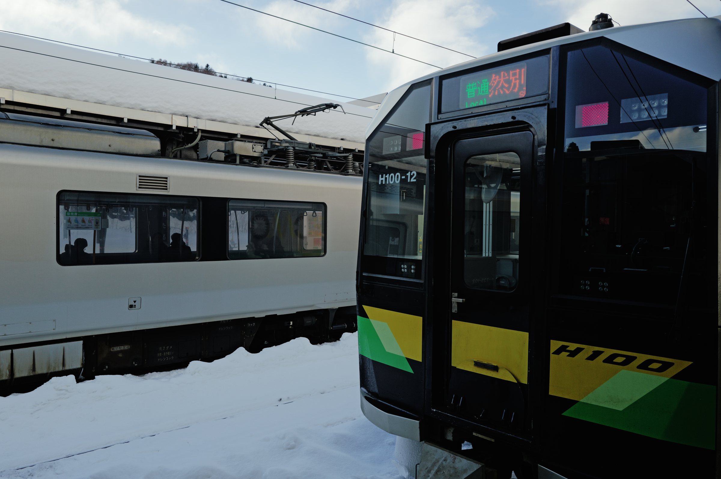 雪のホームに止まる、緑と黄色の気動車