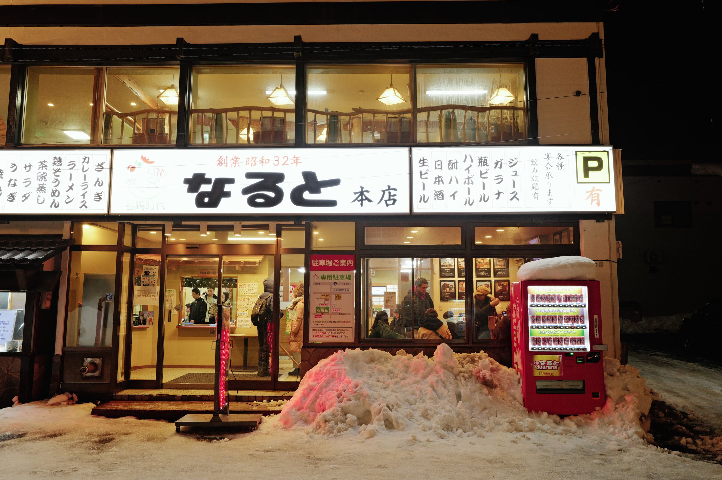 夜、窓いっぱいに灯りのともる店と、店先に積もった雪