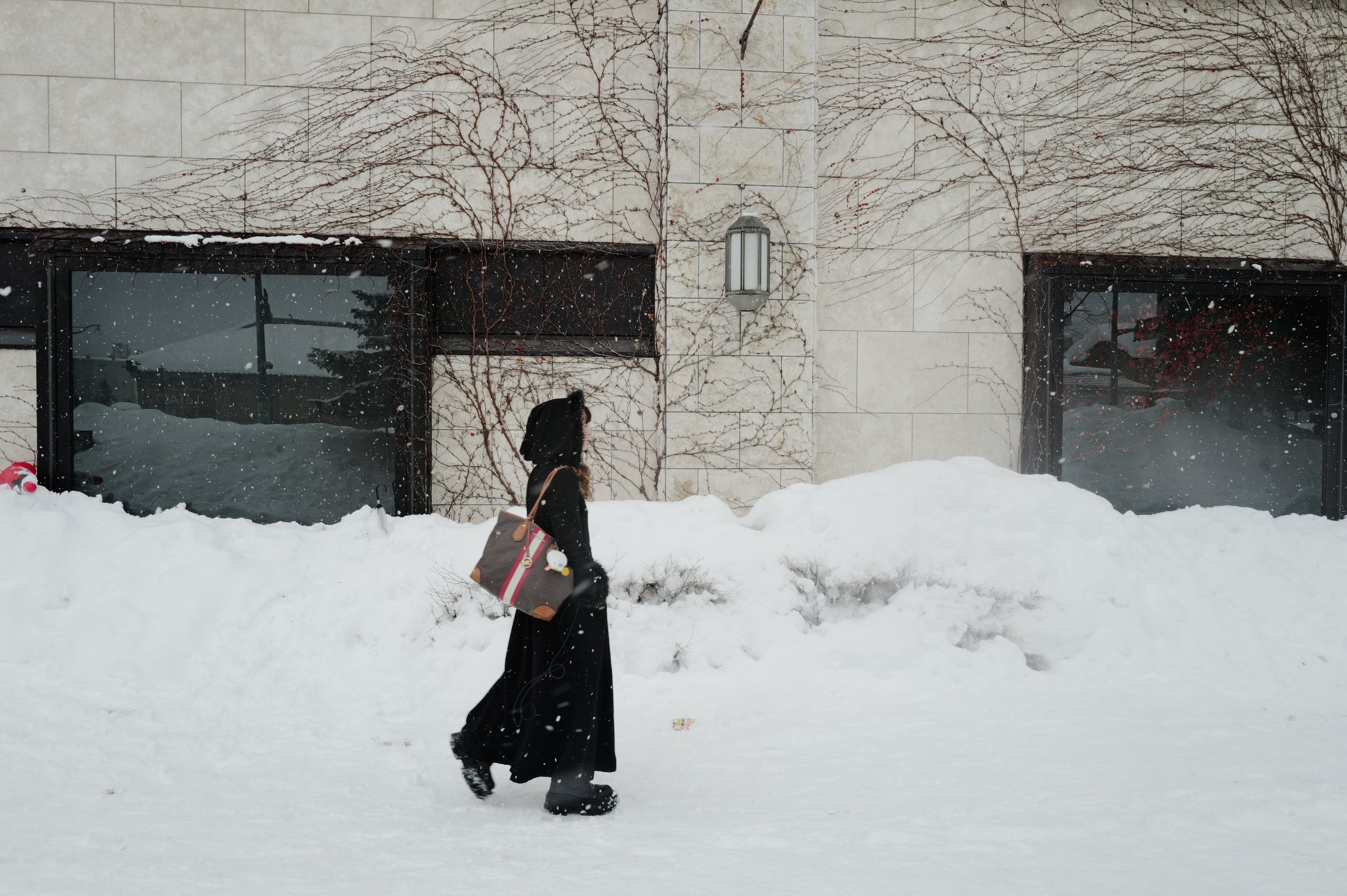 雪の壁のあいだを歩いていく、黒いコートの人