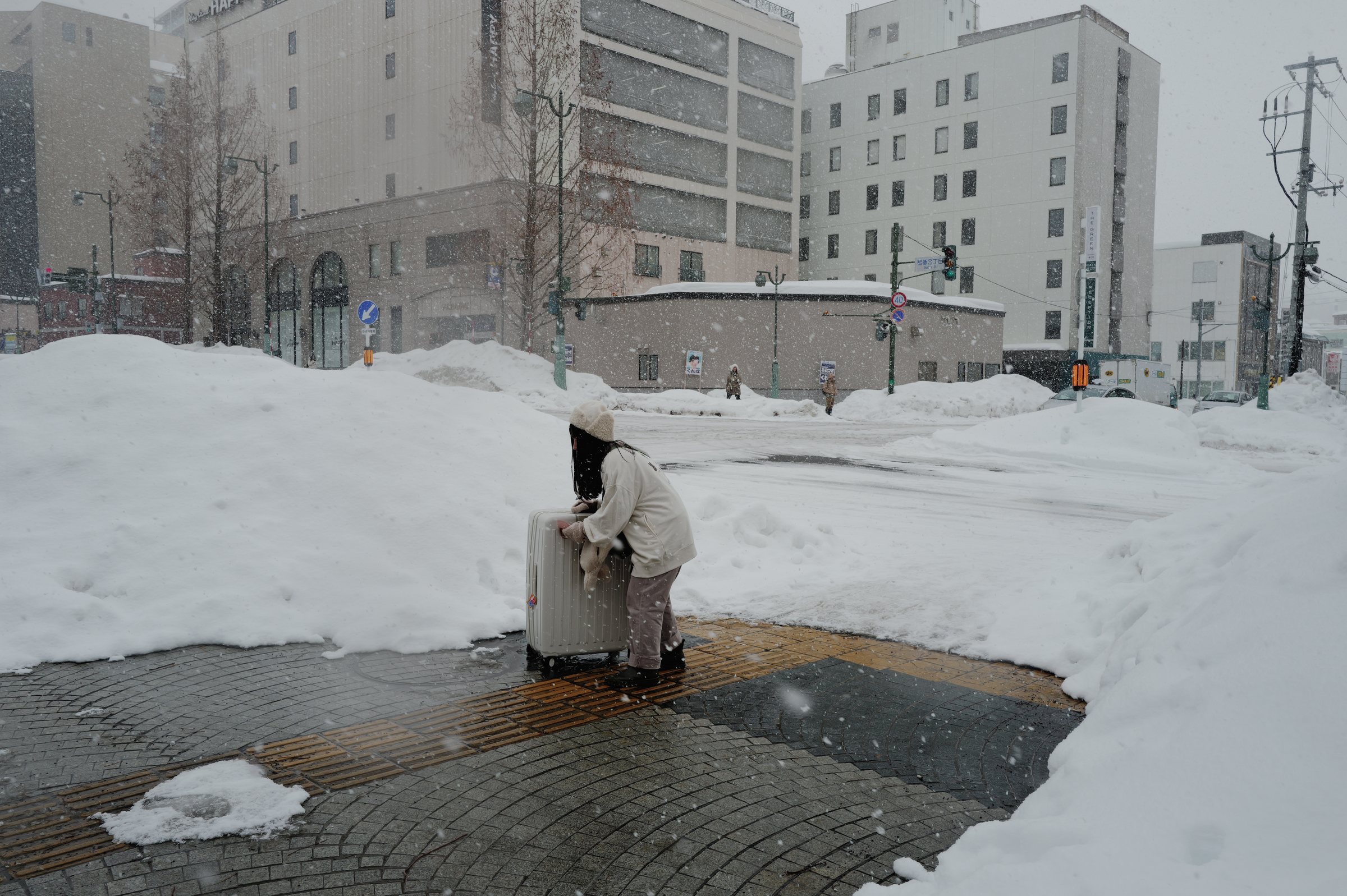 雪の歩道で、スーツケースに両手を置いて寄りかかる人