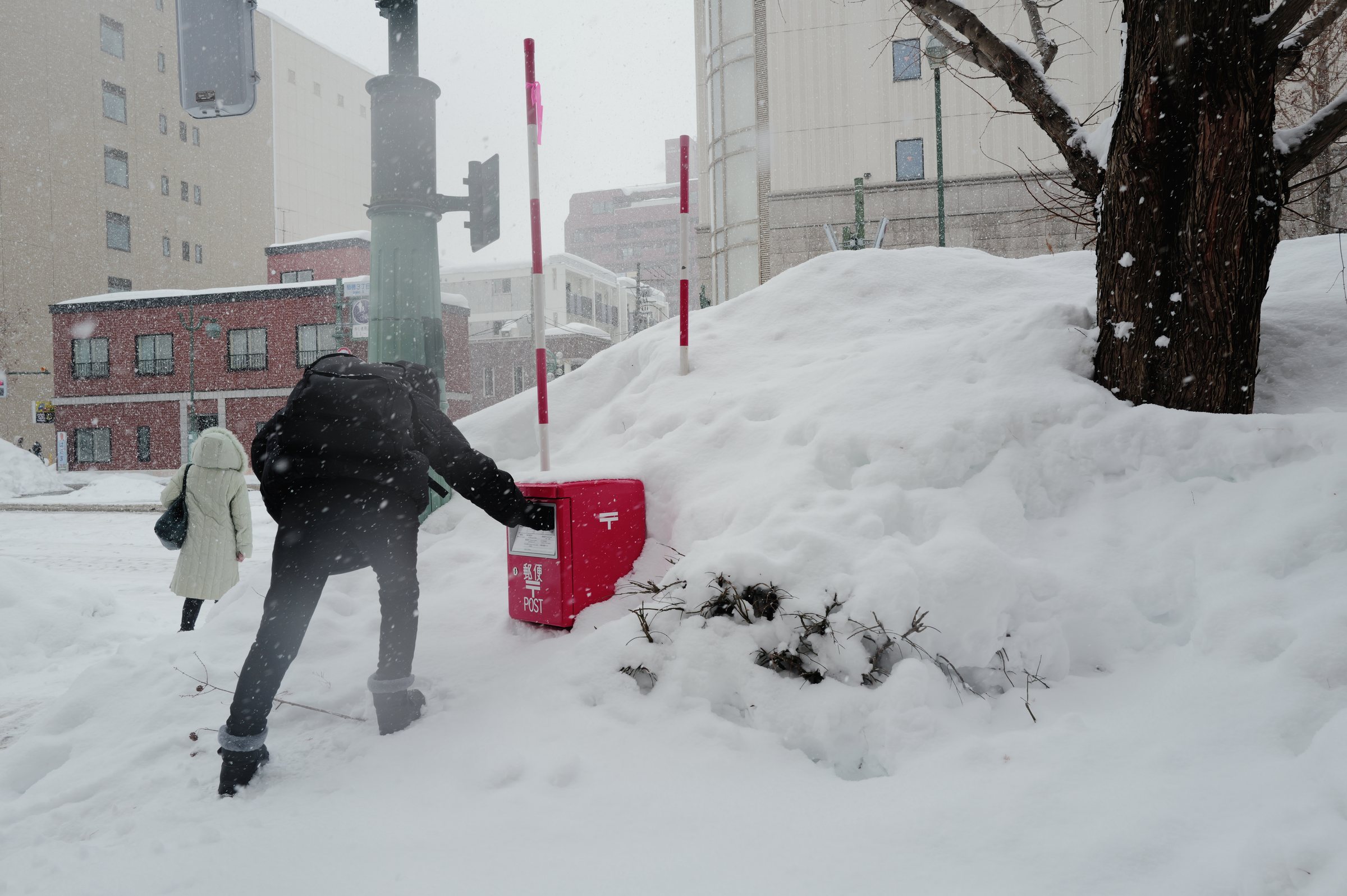 雪に埋もれた赤いポストに、手を伸ばして手紙を入れる人