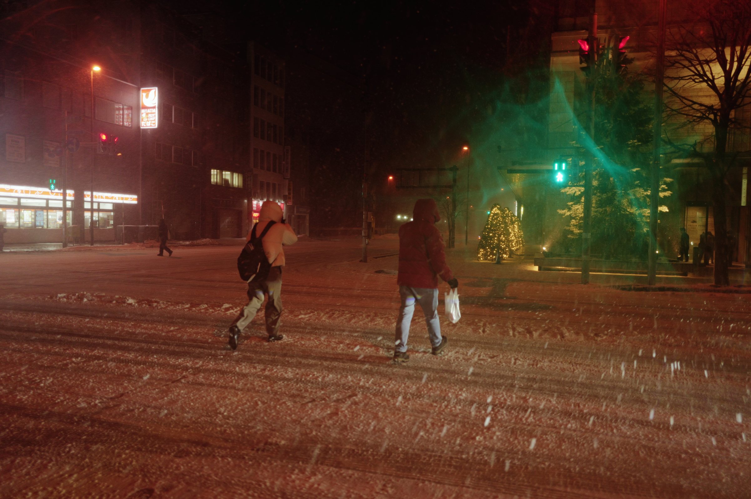雪の夜の交差点を渡る二人