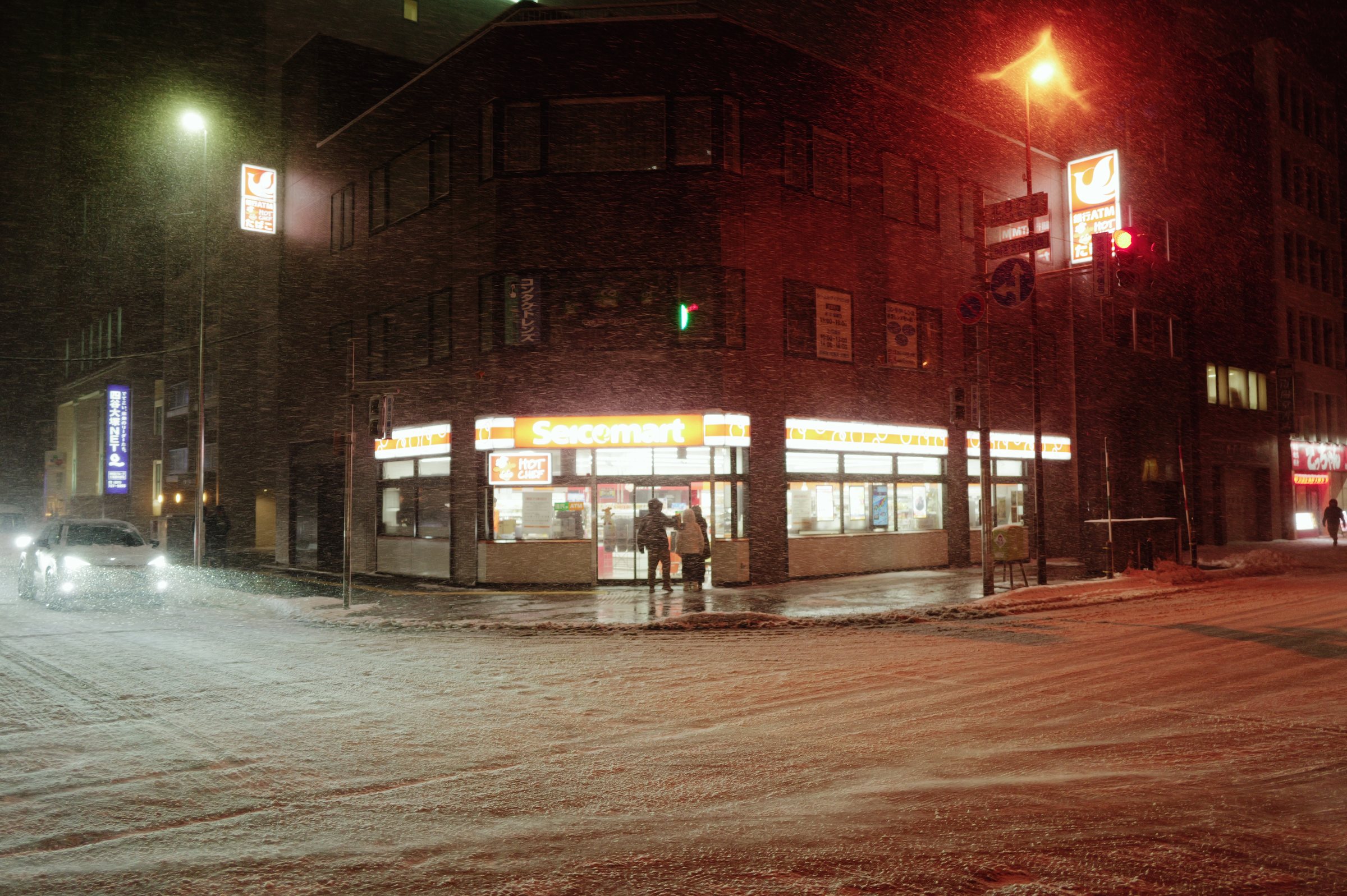 雪の夜、交差点の角で明るく光る店