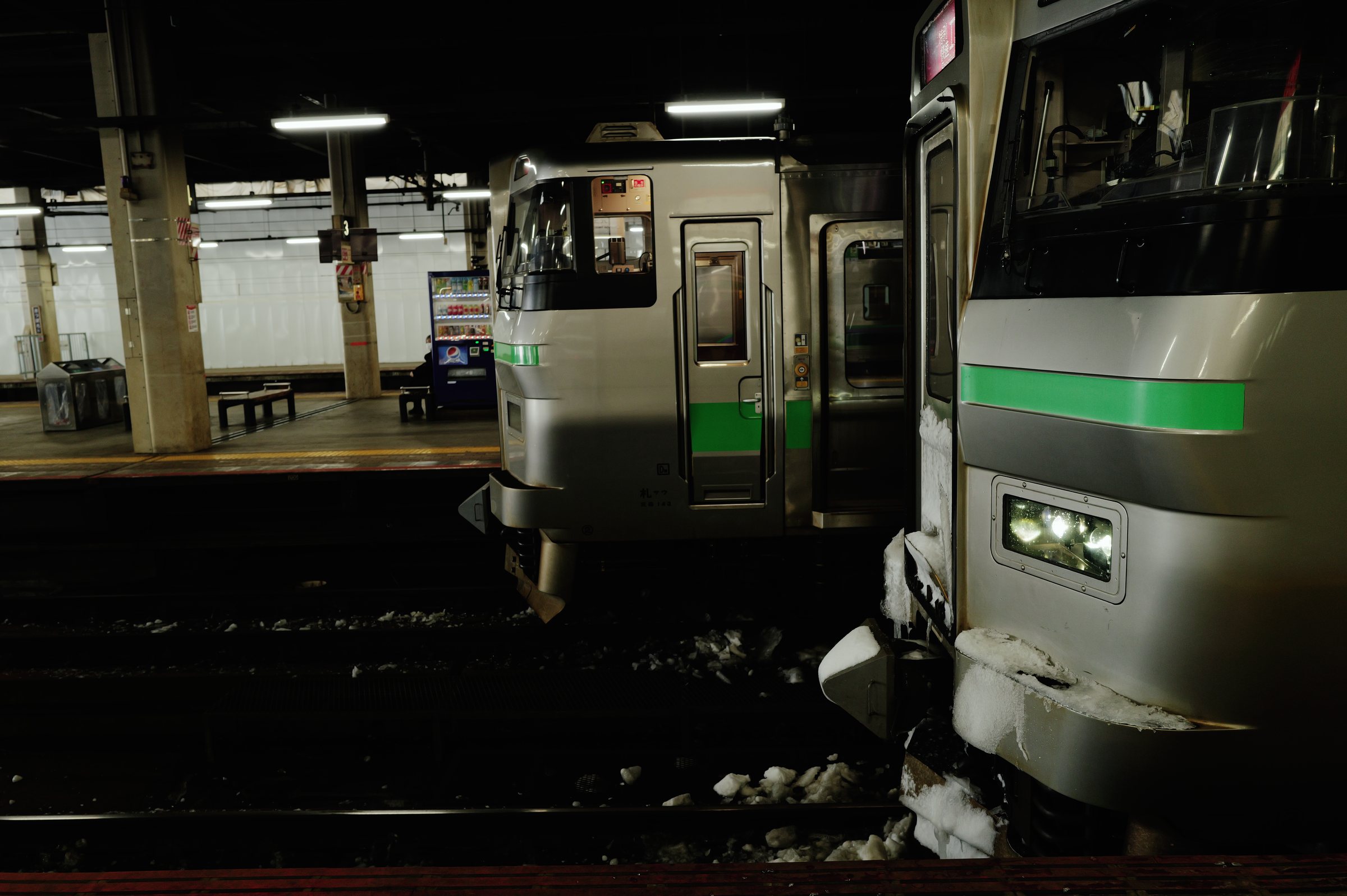 暗い高架のホームに止まる、緑の帯の電車