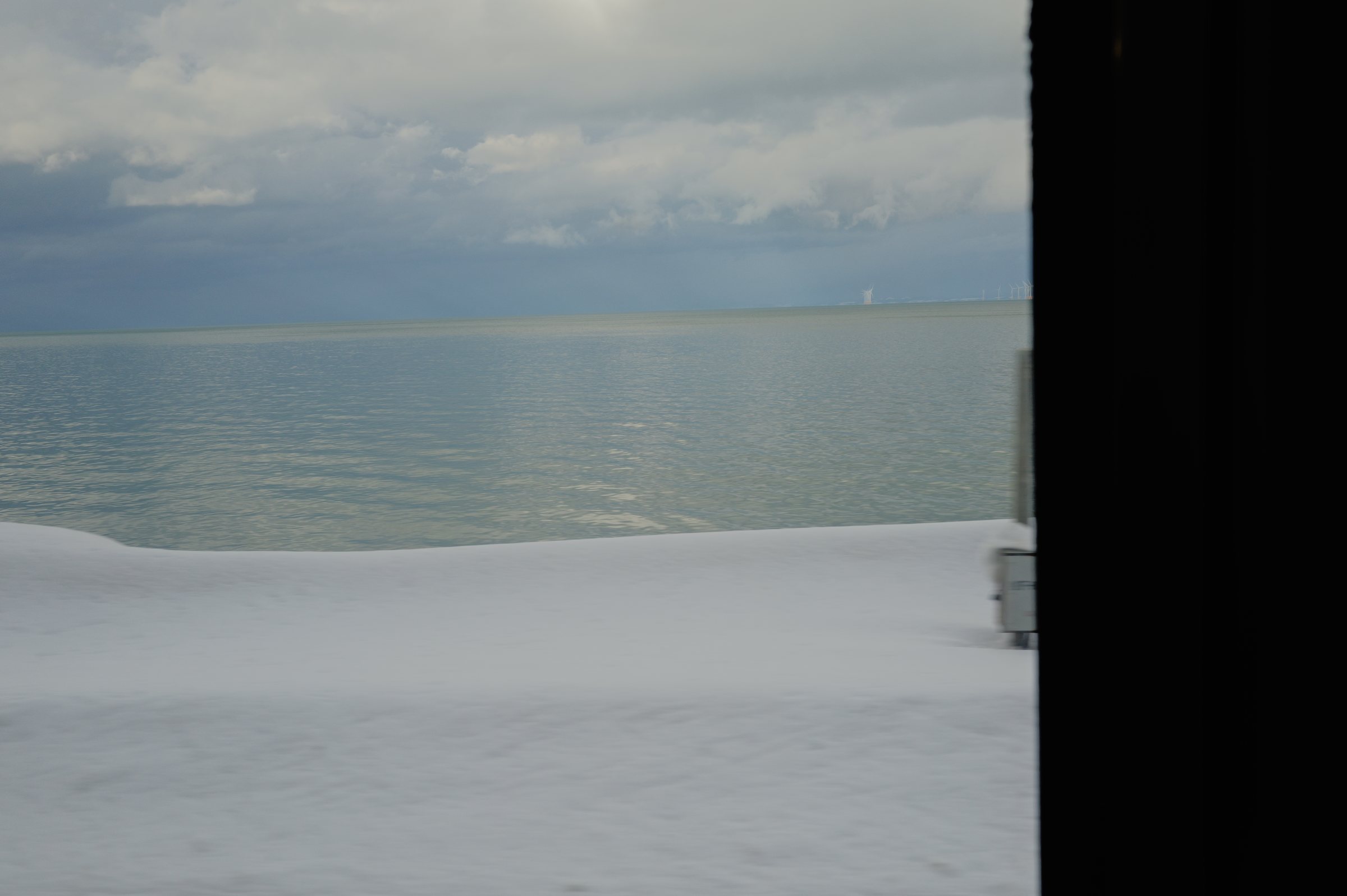 窓枠の脇に広がる、雪の浜と灰色の海