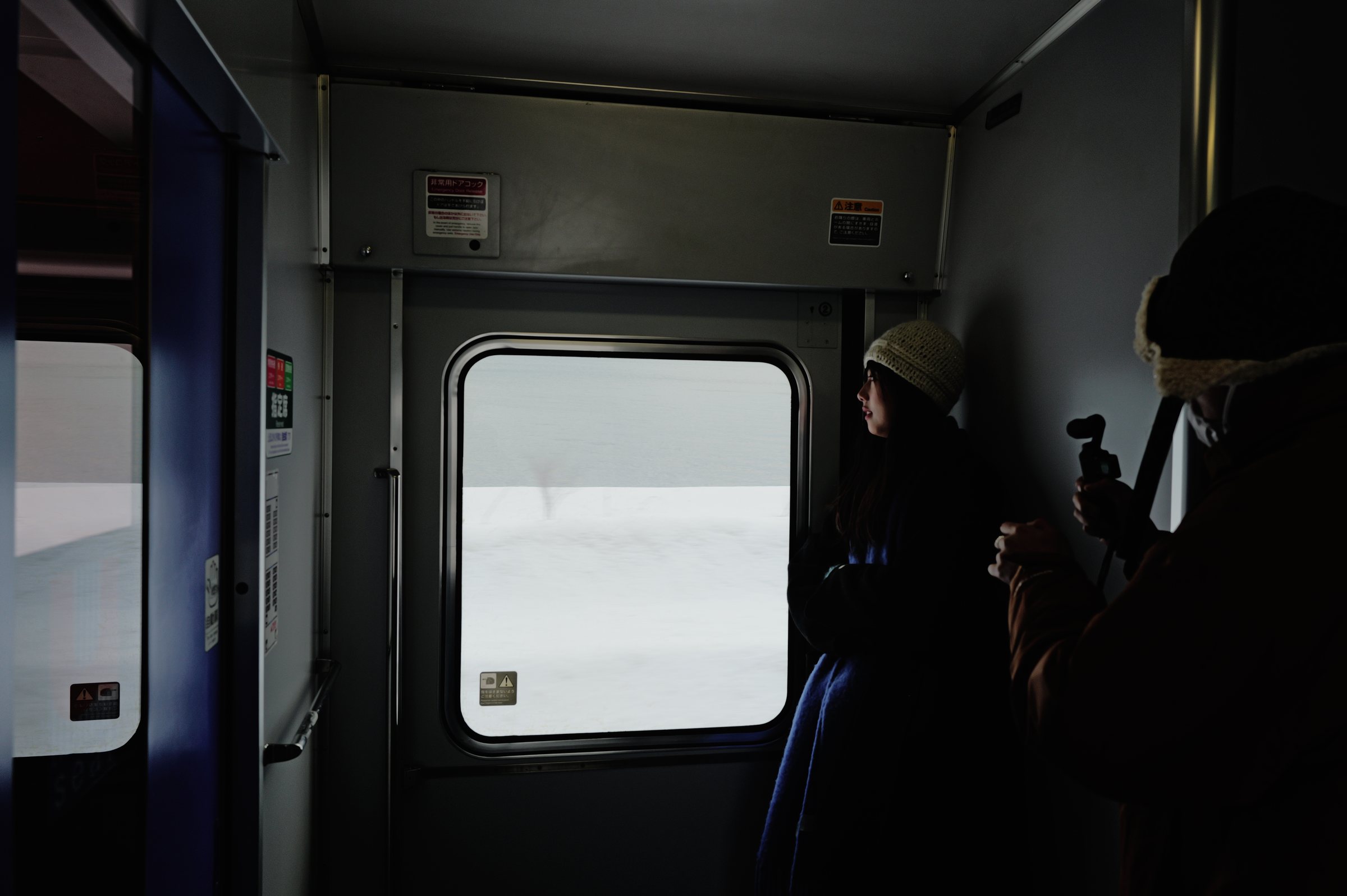 暗い車内のドアの窓に寄る、二人の影と雪の浜