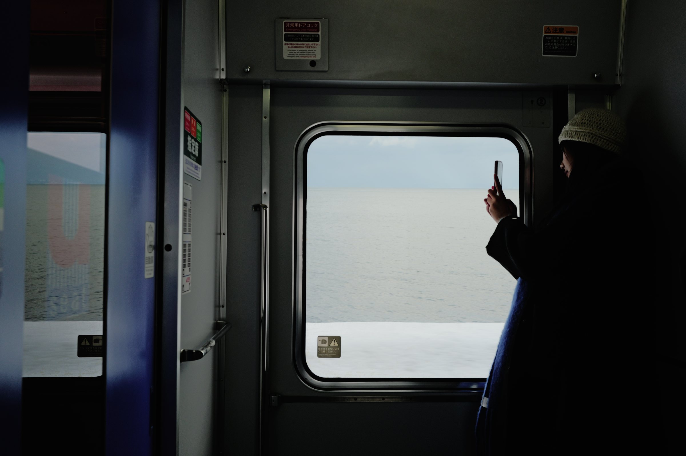 ドアの窓の前で、海を写真に撮る人の影