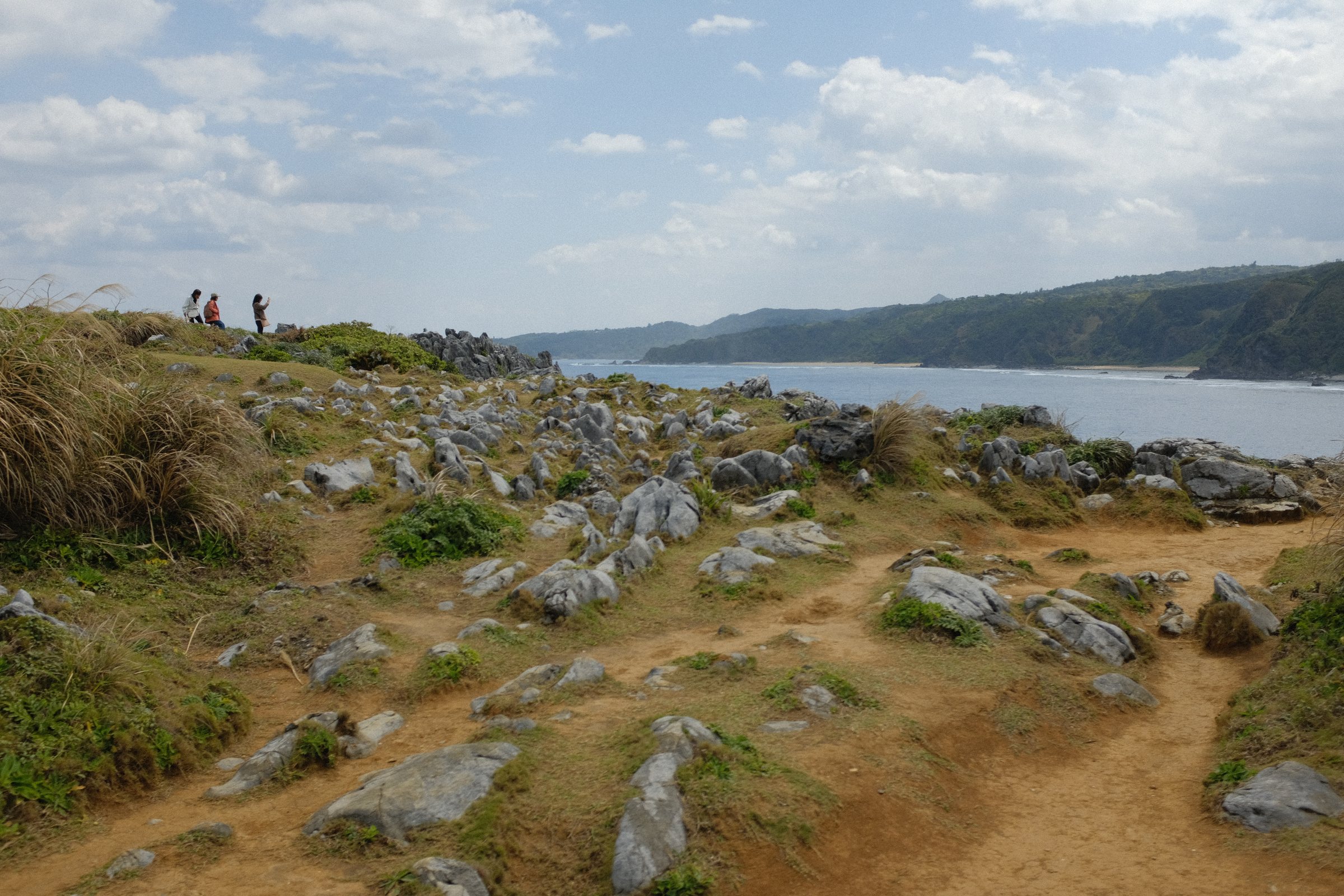 岩の点在する岬の小道と、その先の海と山