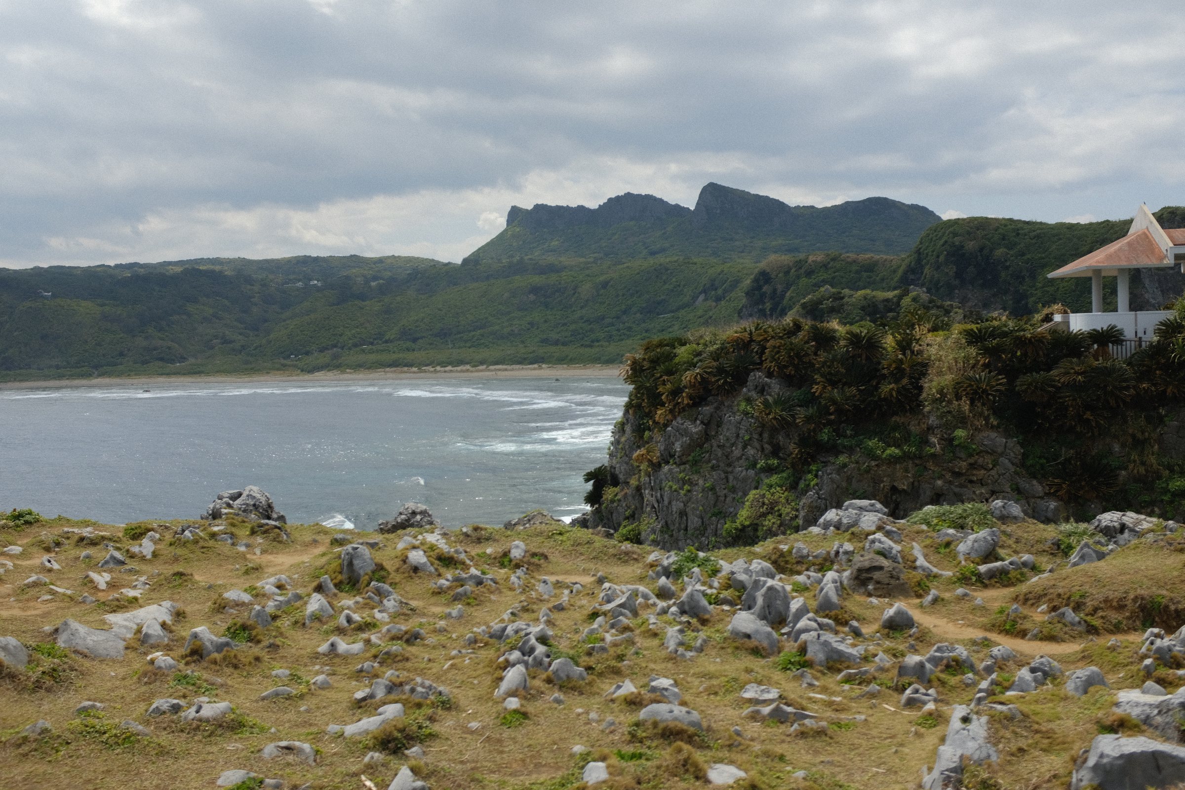 岩の点在する岬の草地と、その向こうに切り立つ山