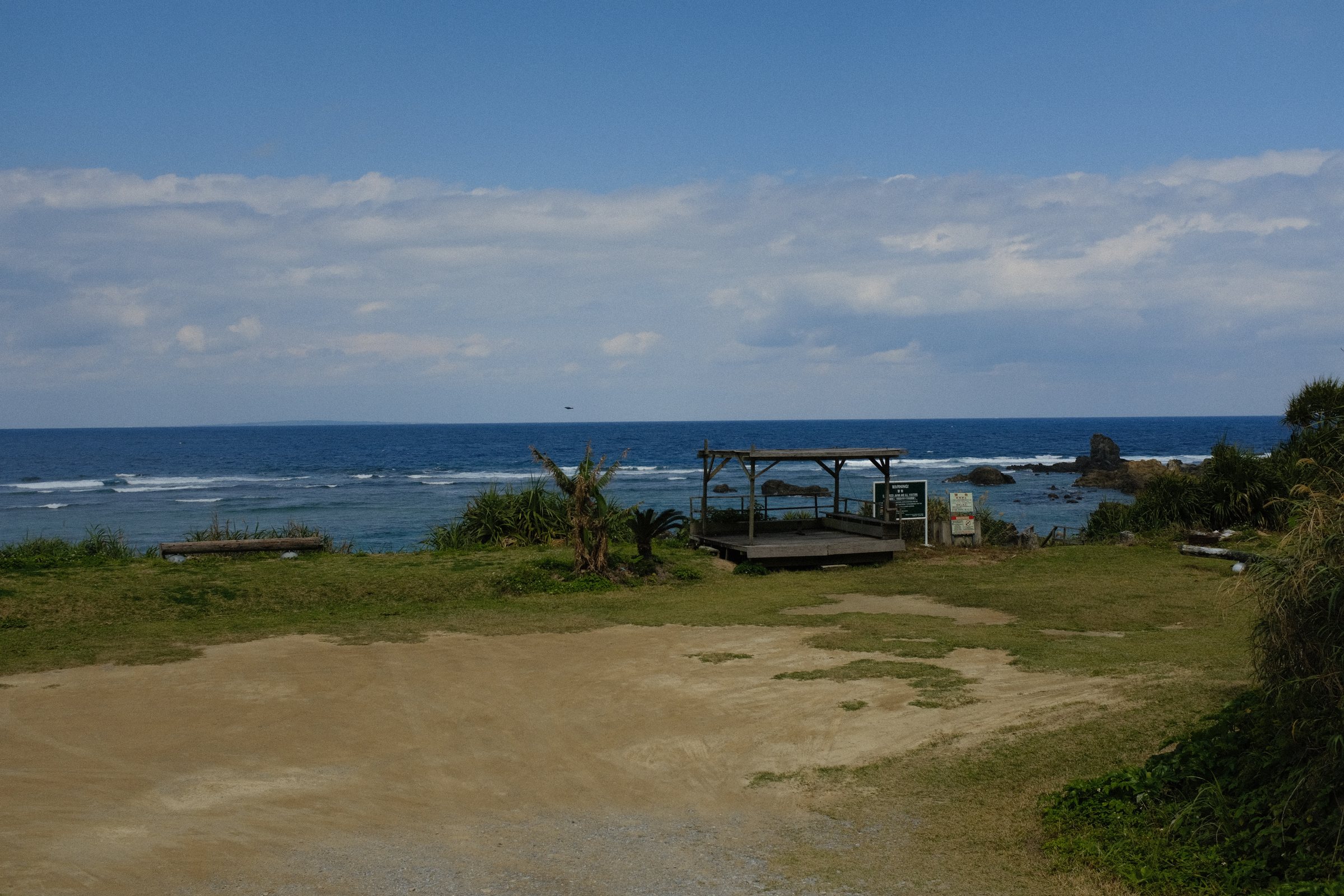 草地の先の東屋と、白い波の立つ外海