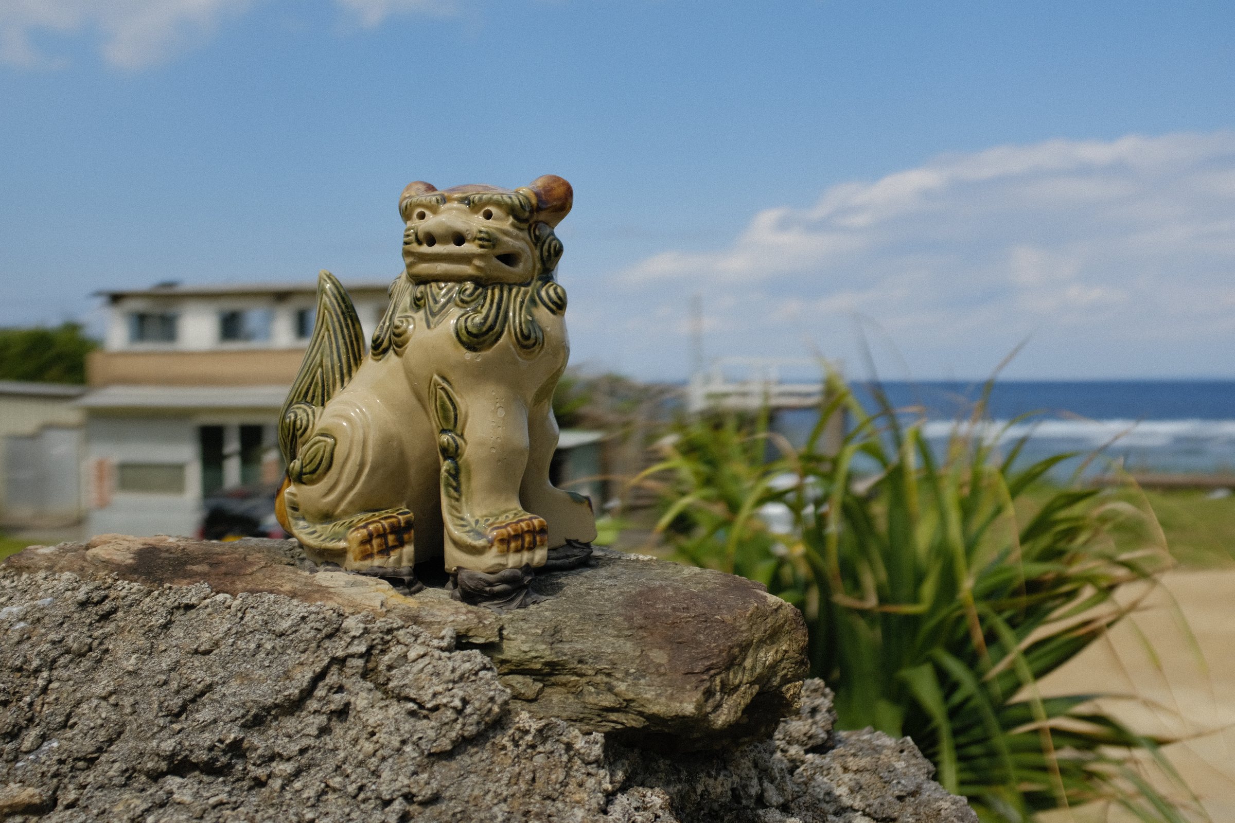 岩の上に置かれた小さなシーサーと、海辺の家