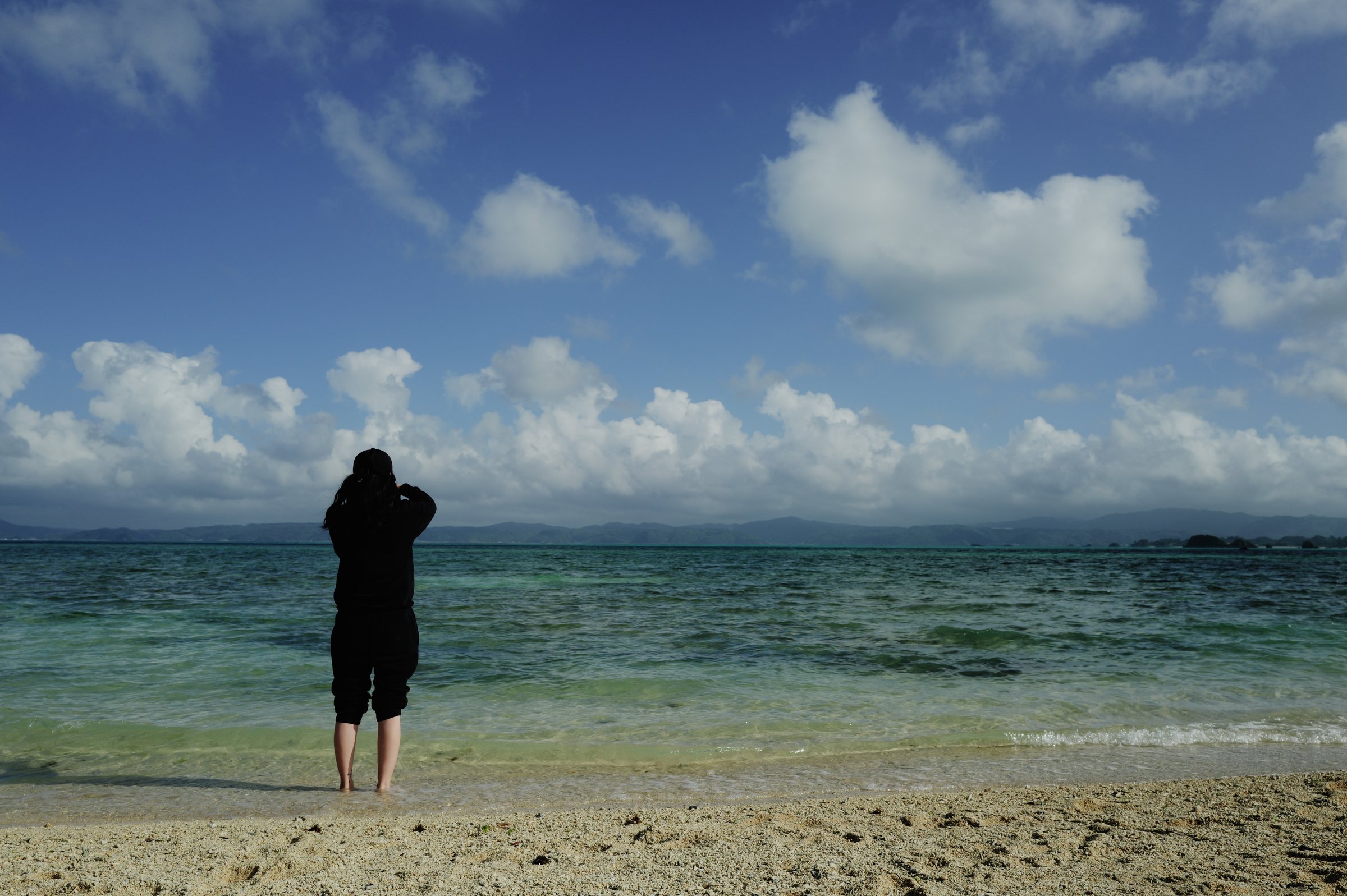 波打ち際に立ち、海のほうを向く人の後ろ姿