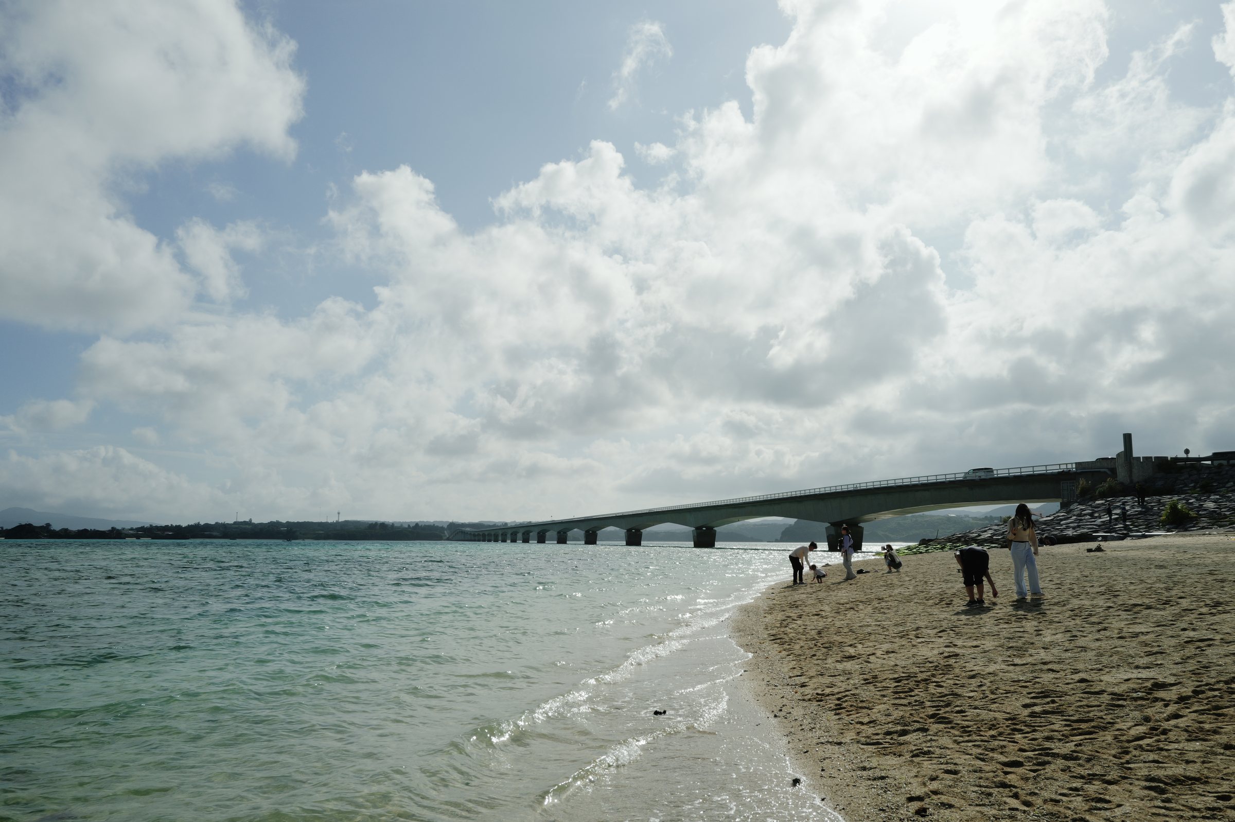 波打ち際の向こうに延びる長い橋と、浜を歩く人たち