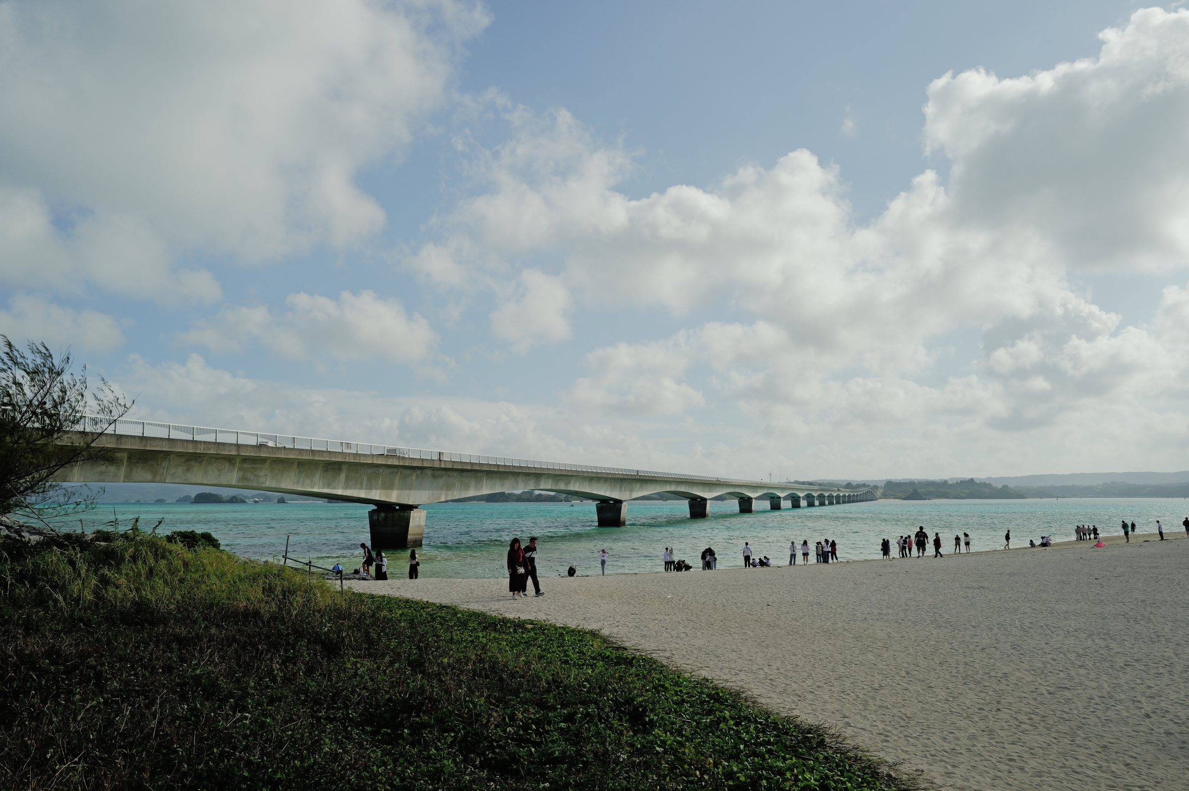 浜の向こうに延びる長い橋と、浜を歩く人たち