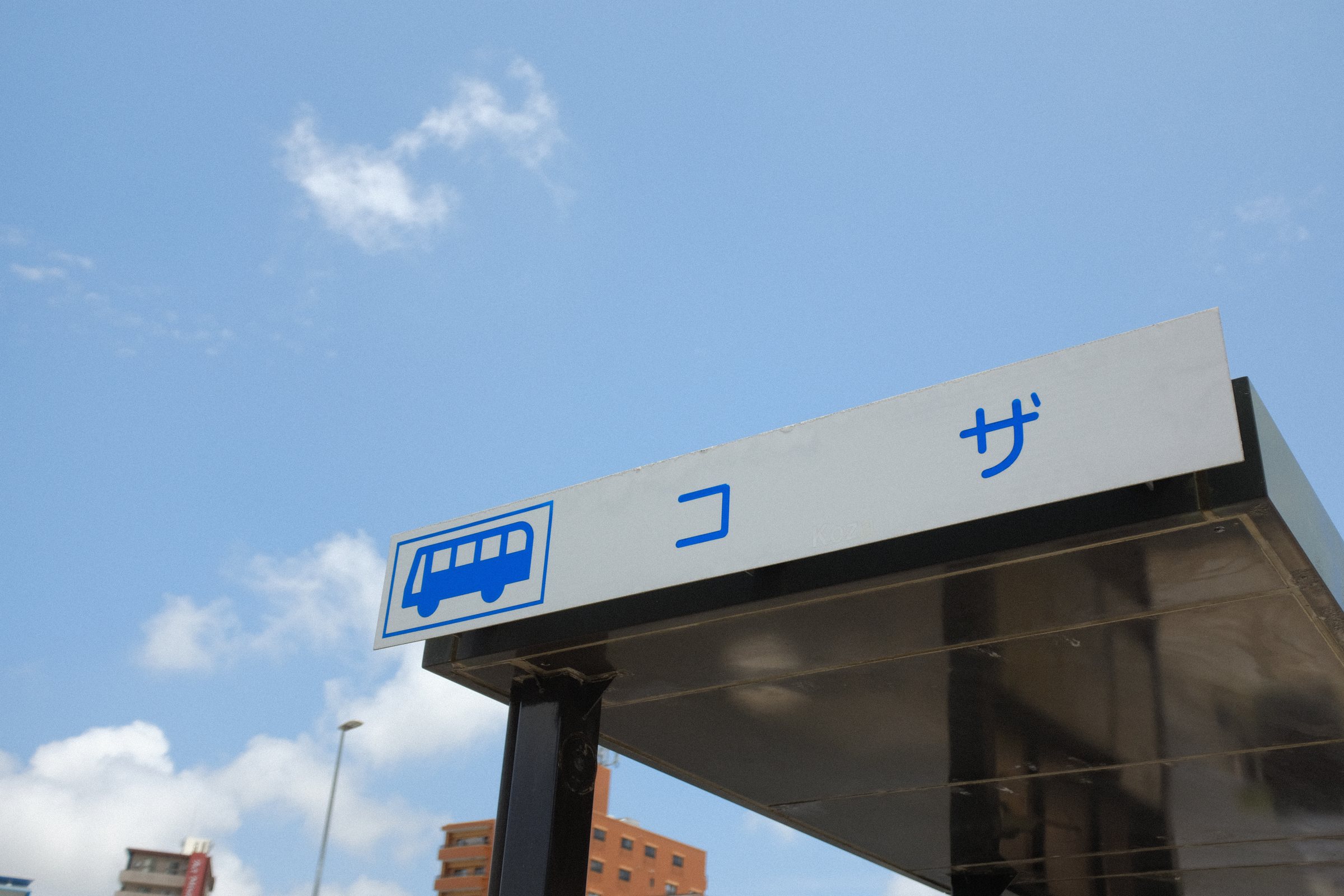青空の下、「コザ」と書かれたバス停の屋根