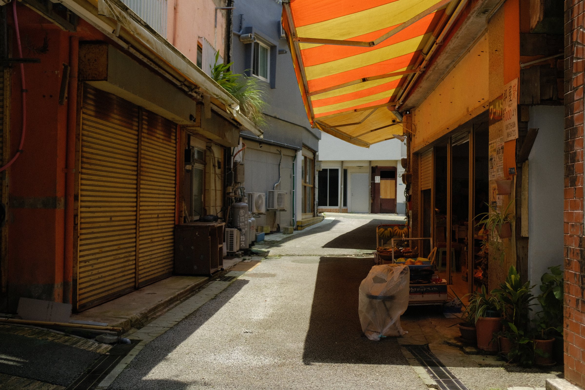 オレンジと黄色の縞の日除けがかかる、シャッターの路地