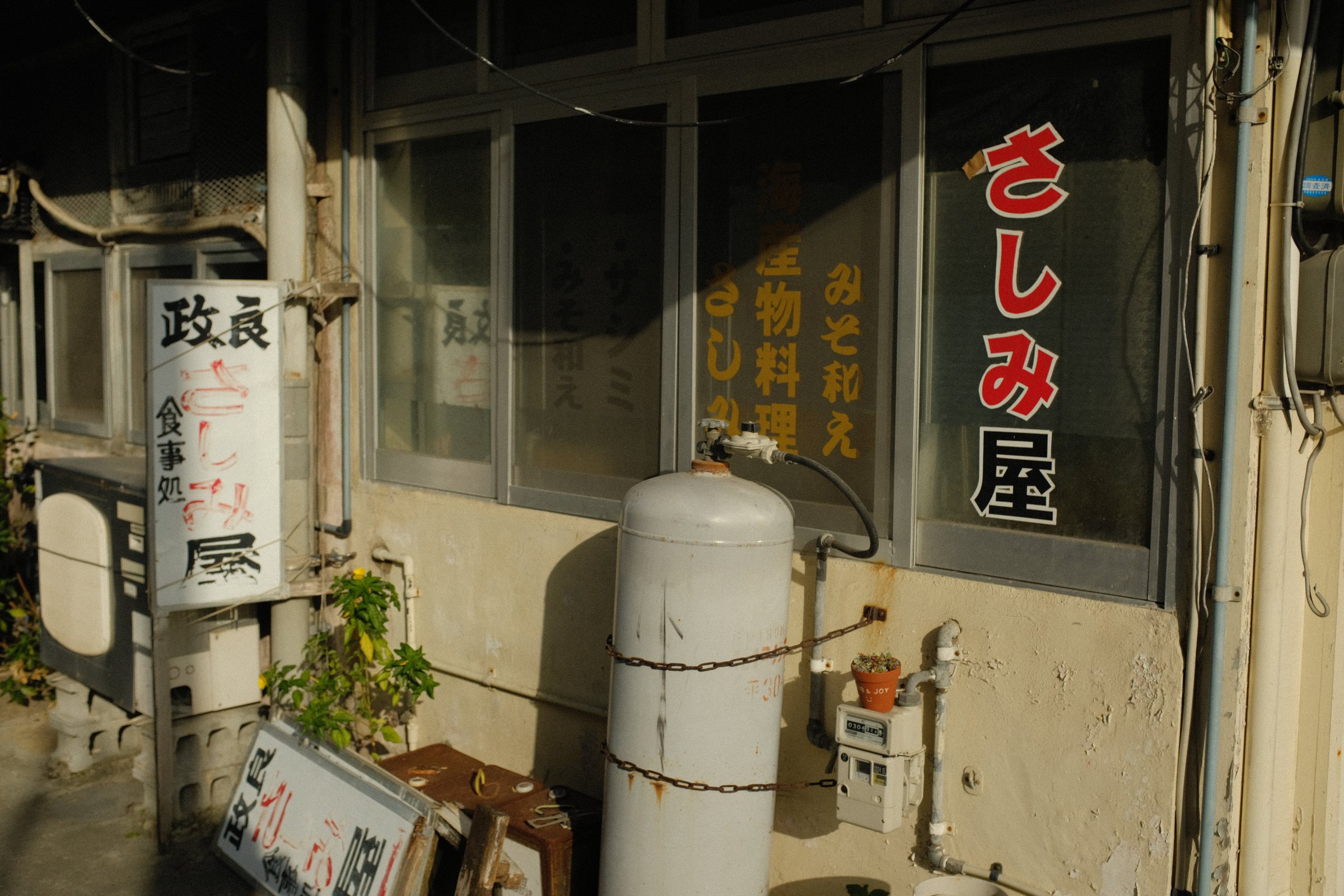 ガスボンベの脇に看板の掛かる、さしみ屋の入口