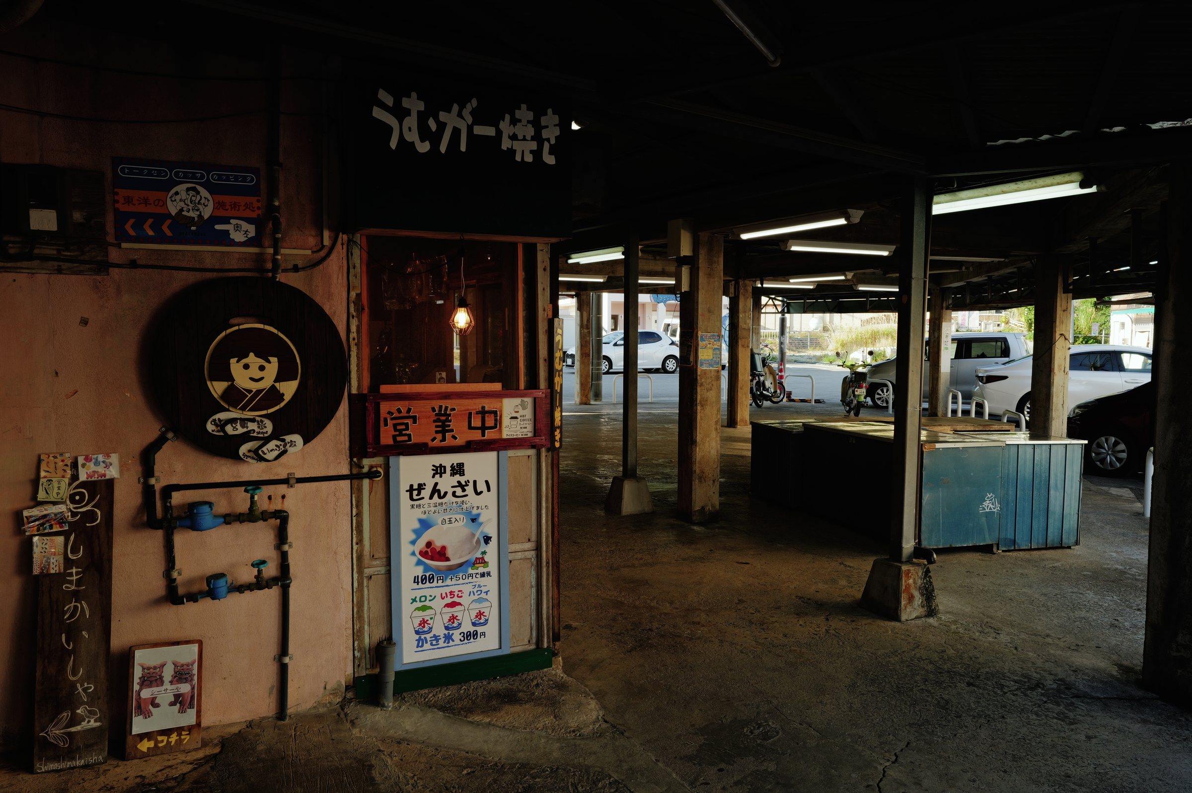 薄暗い市場の柱に掛かる、ぜんざいの店の看板と灯り