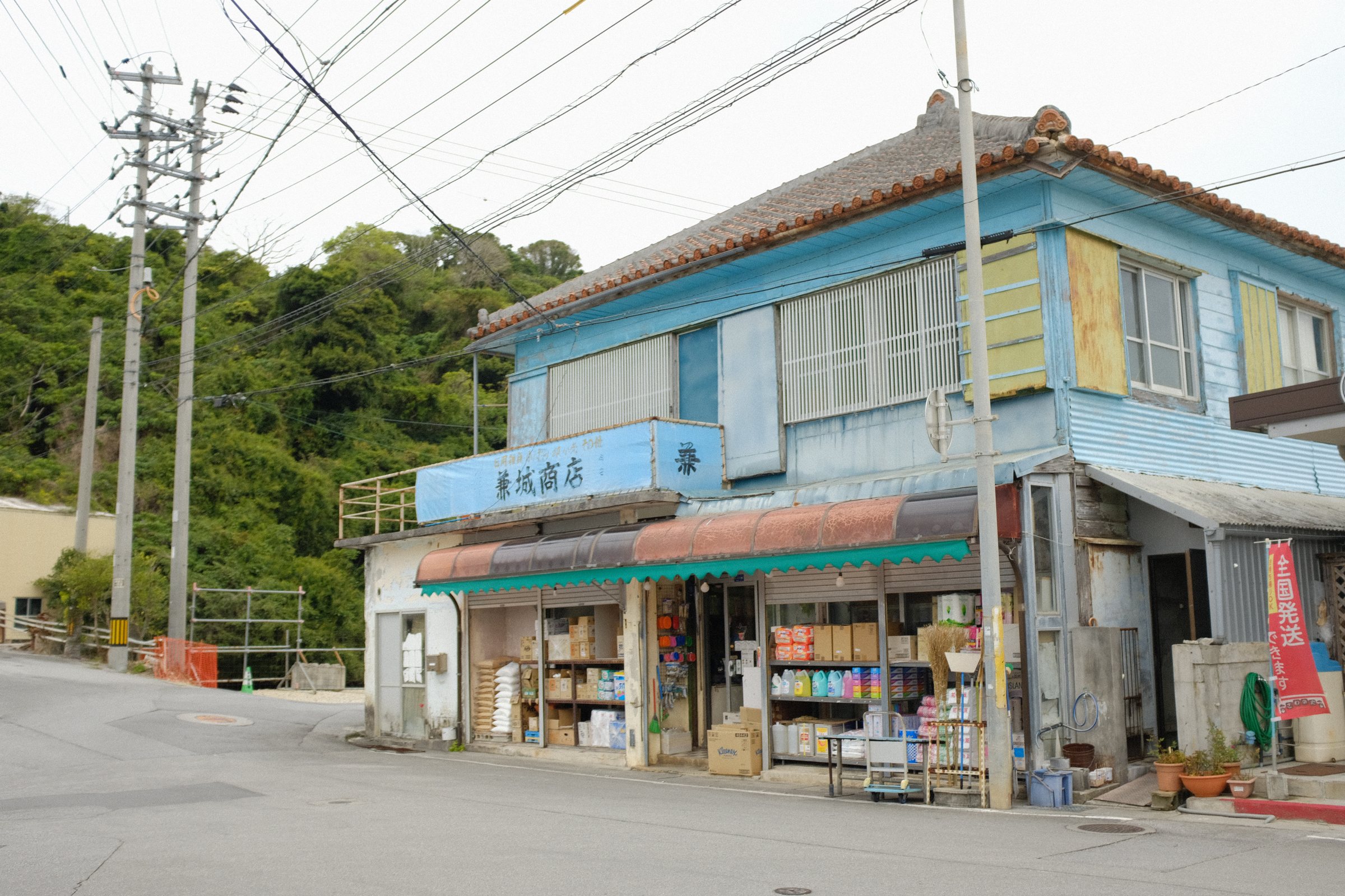 青い二階建ての古い商店と、店先に並ぶ品物