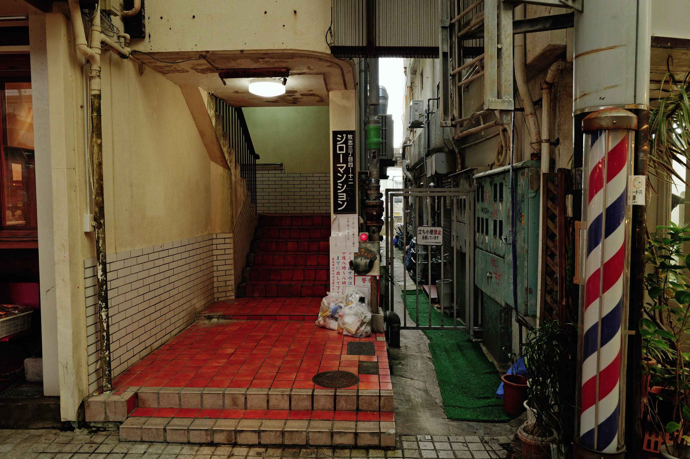 赤いタイルの階段と、路地に立つ床屋のポール