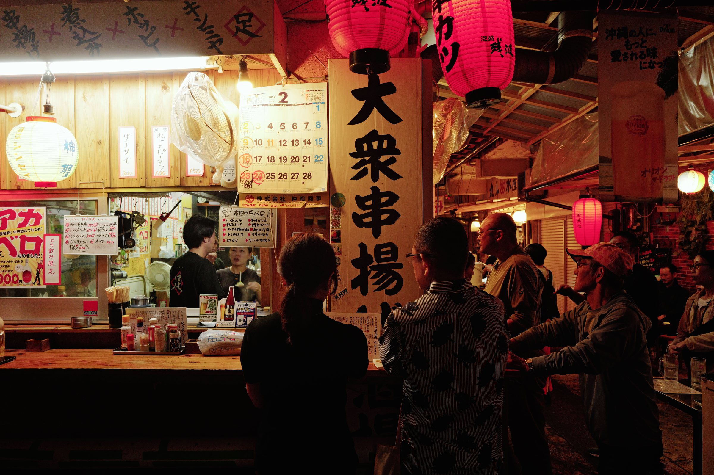 提灯の下がる串揚げの店のカウンターと、集まった人の影