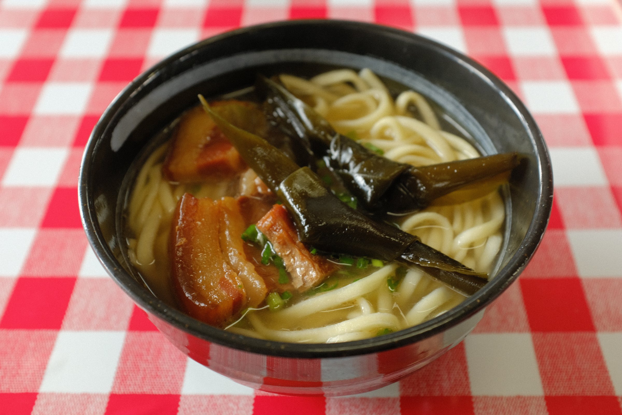 赤と白のチェックのクロスの上の、三枚肉と昆布の沖縄そば