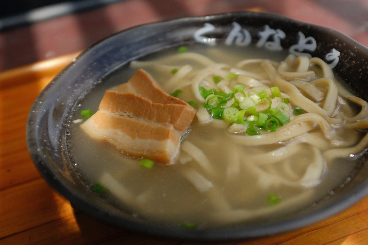店の名前が入った黒い器の沖縄そばと、のせられた三枚肉と葱