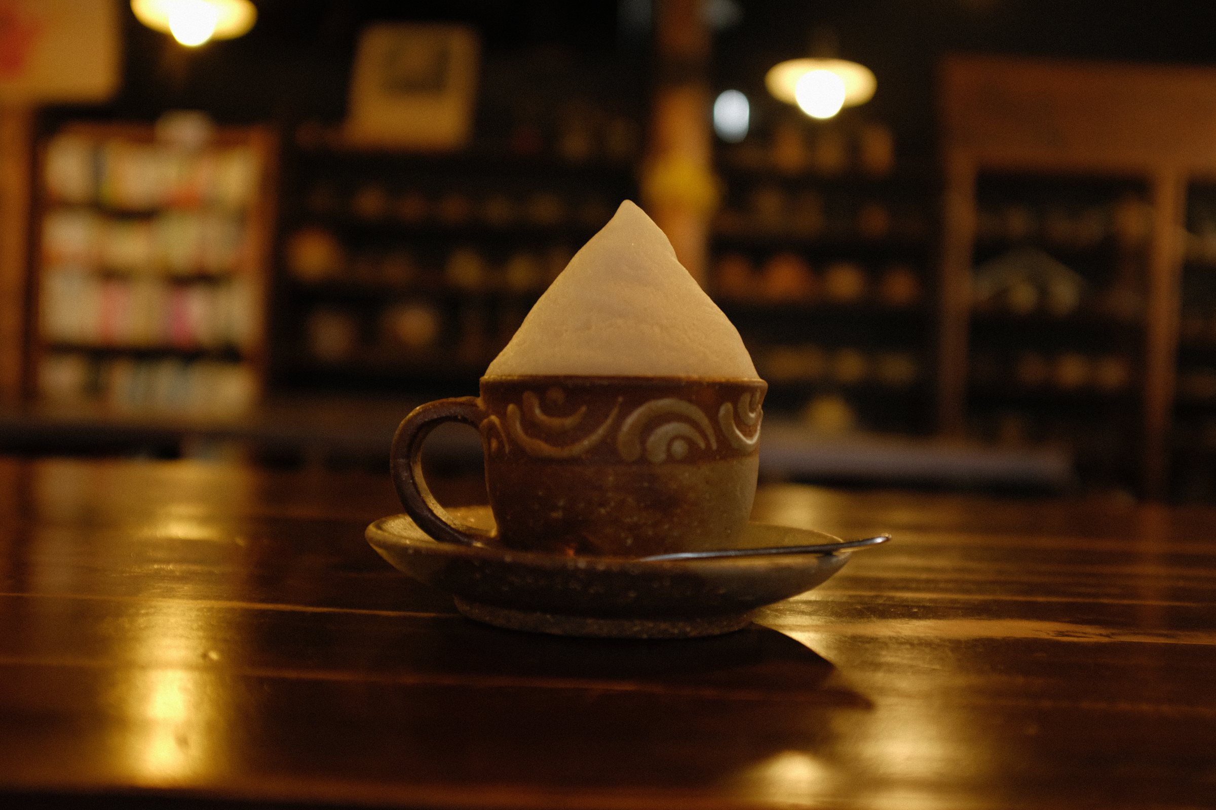 暗い喫茶店のテーブルに置かれた、泡が三角に立つカップ
