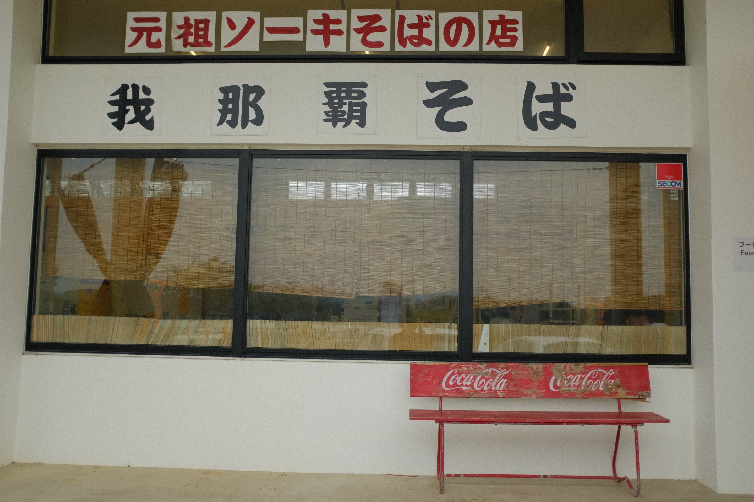 「元祖ソーキそばの店」「我那覇そば」の看板と赤いベンチ