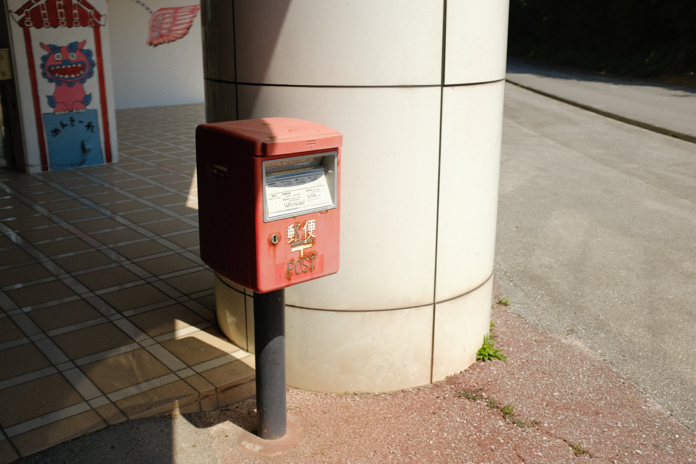 白い柱の脇に立つ赤いポスト
