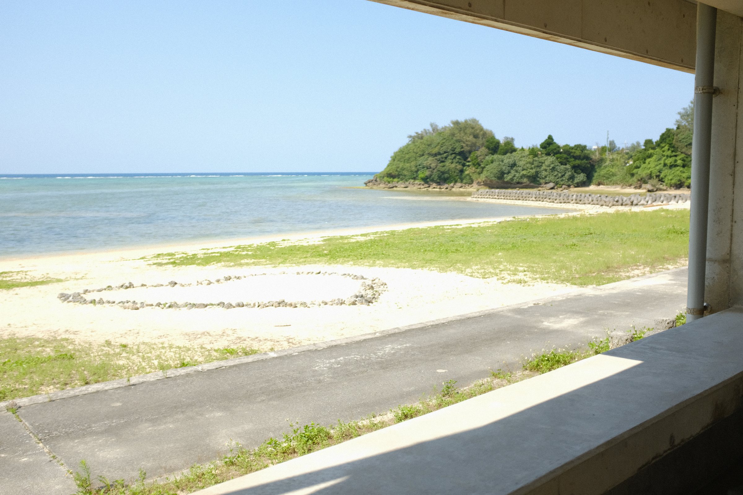 建物の窓枠越しに見る、白い浜と緑の小島