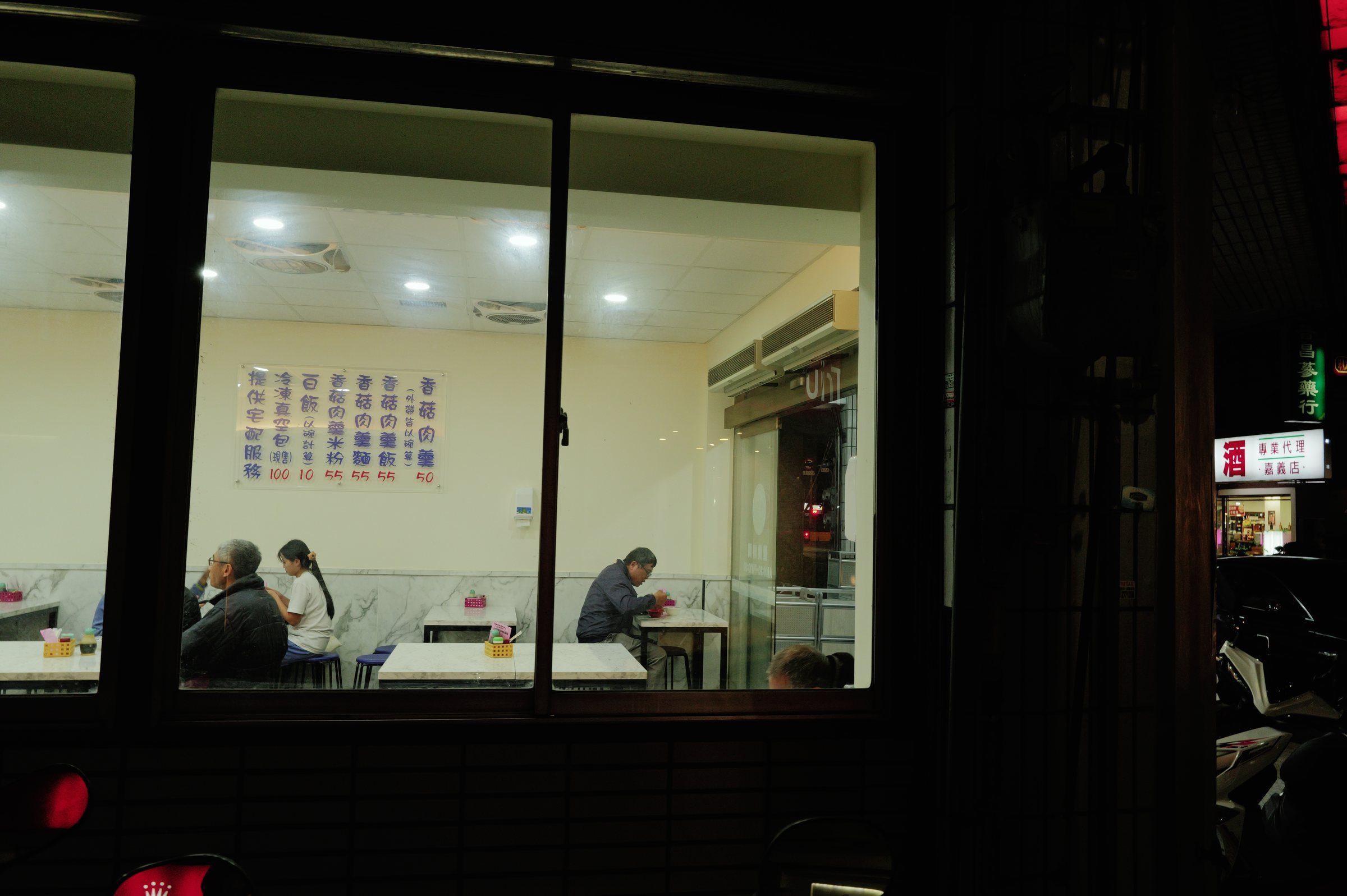 夜の食堂の大きな窓の中で、向かい合って食事をする二人