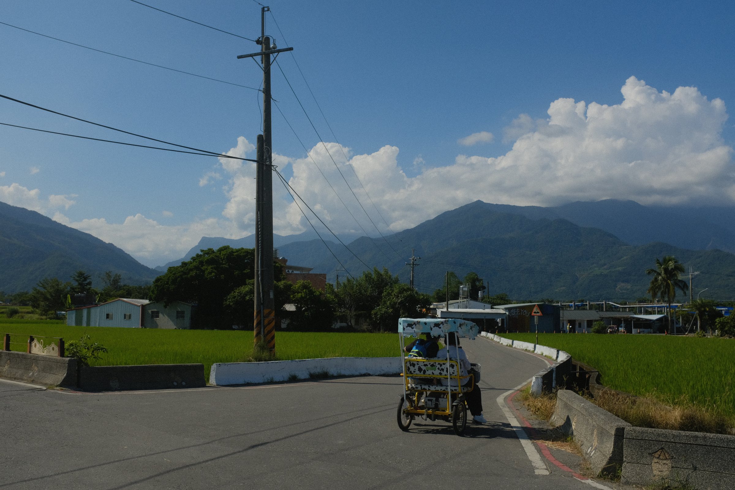 電柱の脇を通り過ぎる三輪の自転車と、山にかかる雲