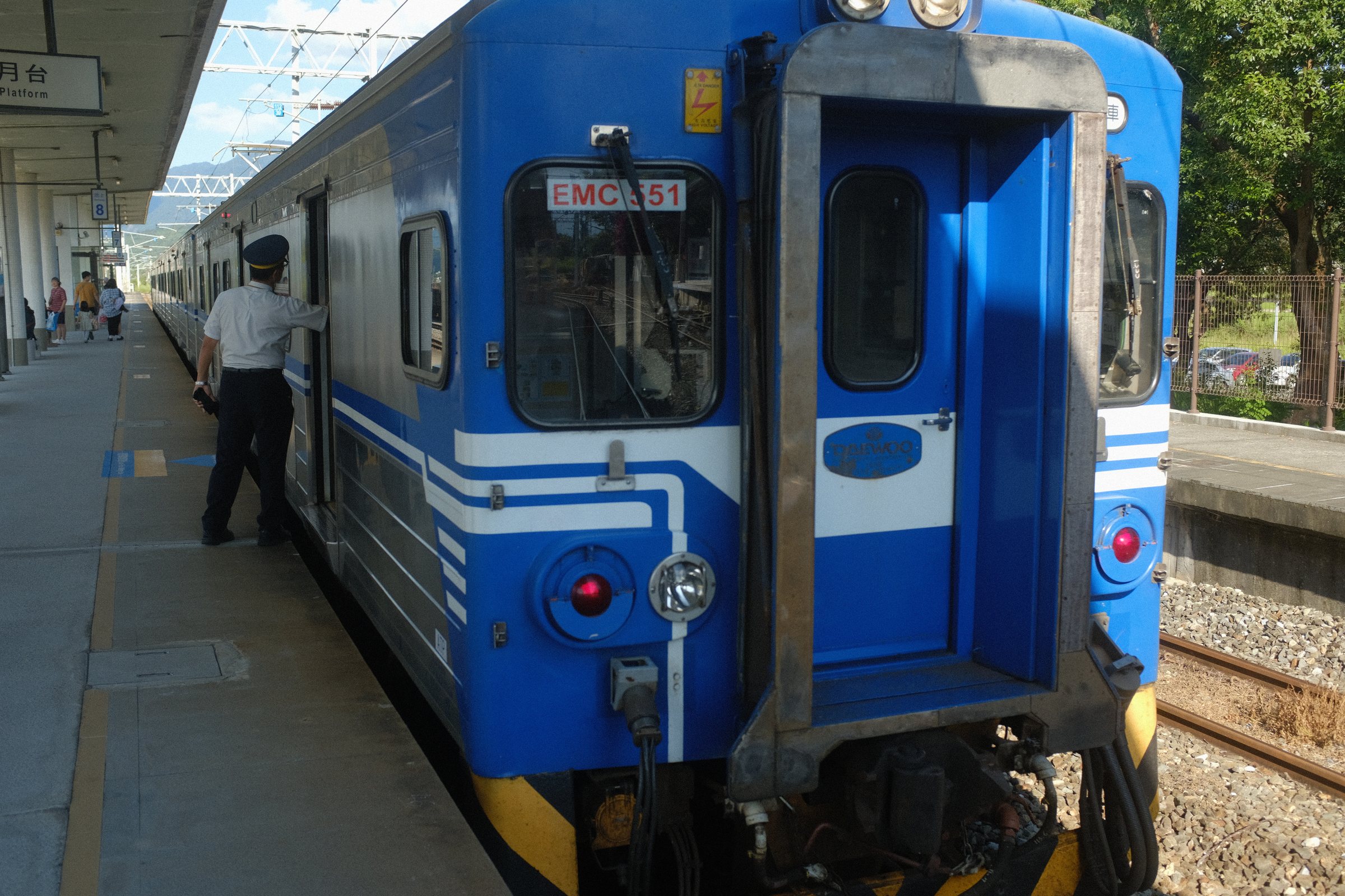 ホームに止まる青い列車と、扉の前に立つ車掌