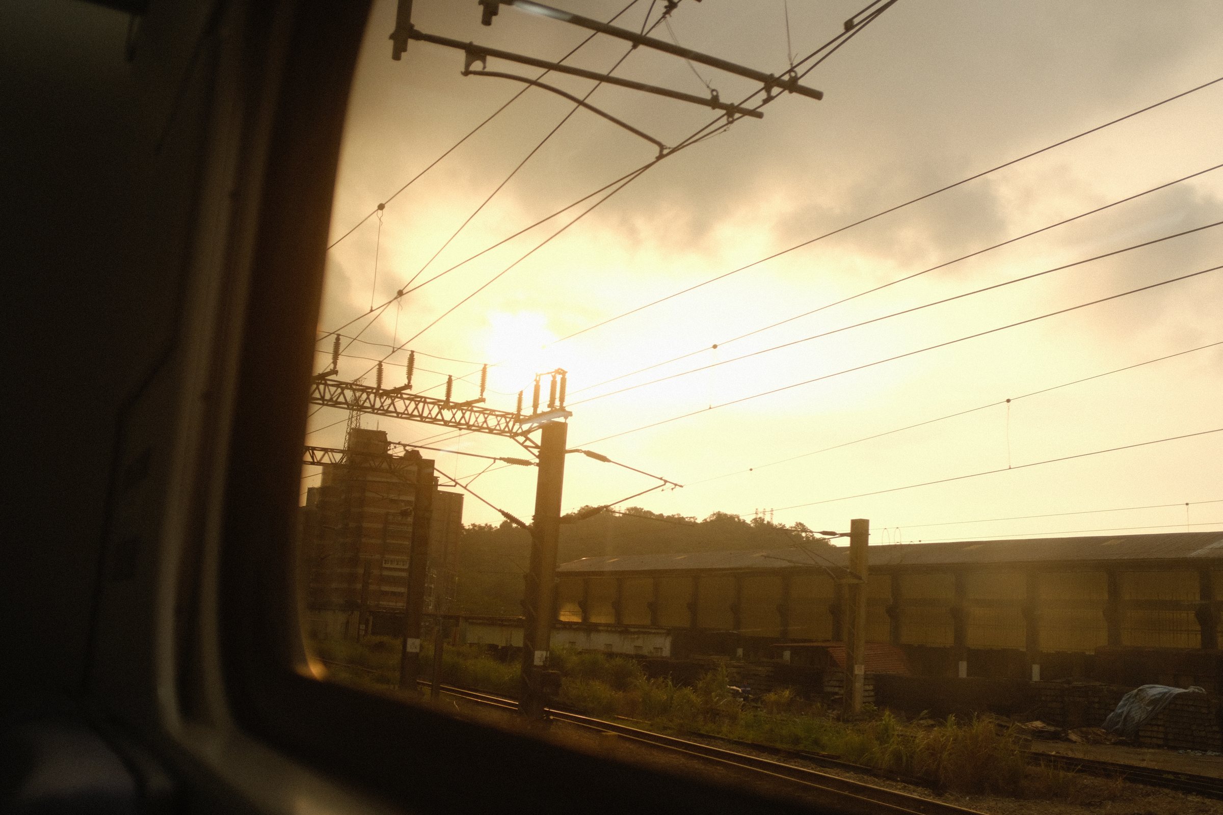 列車の窓枠の中で、架線の向こうに沈む夕陽