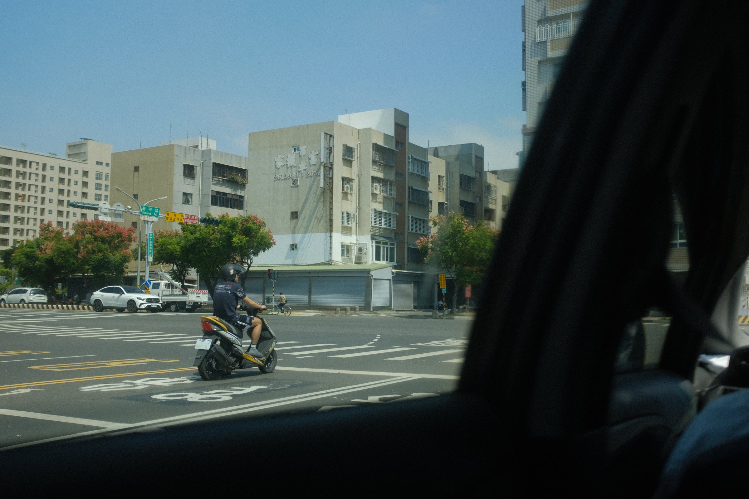 車の窓枠の向こうで、交差点を渡るバイク