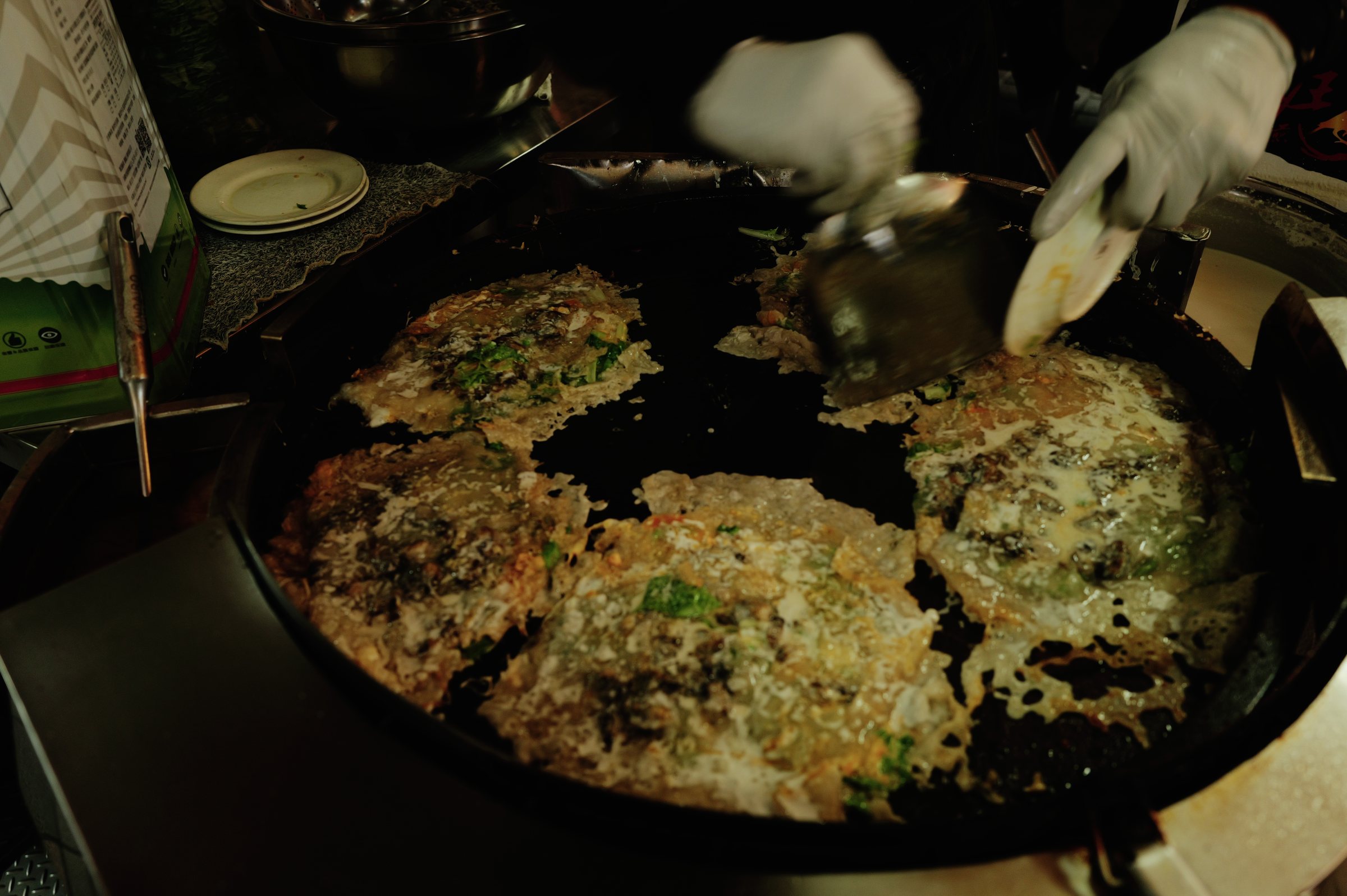 大きな鉄板の上で焼かれる何枚もの蚵仔煎と、へらを持つ手