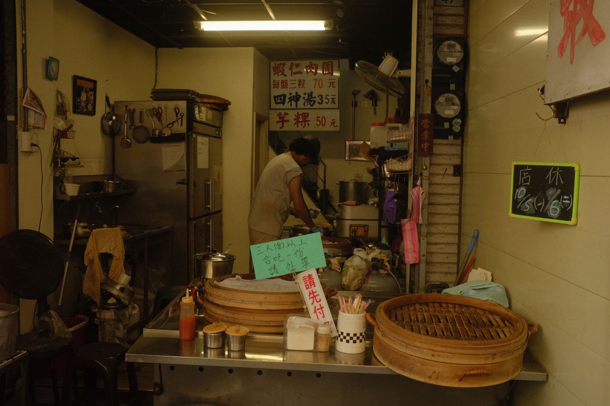 夕方の食堂の厨房。蒸籠と鍋が並び、奥に店の人が立っている