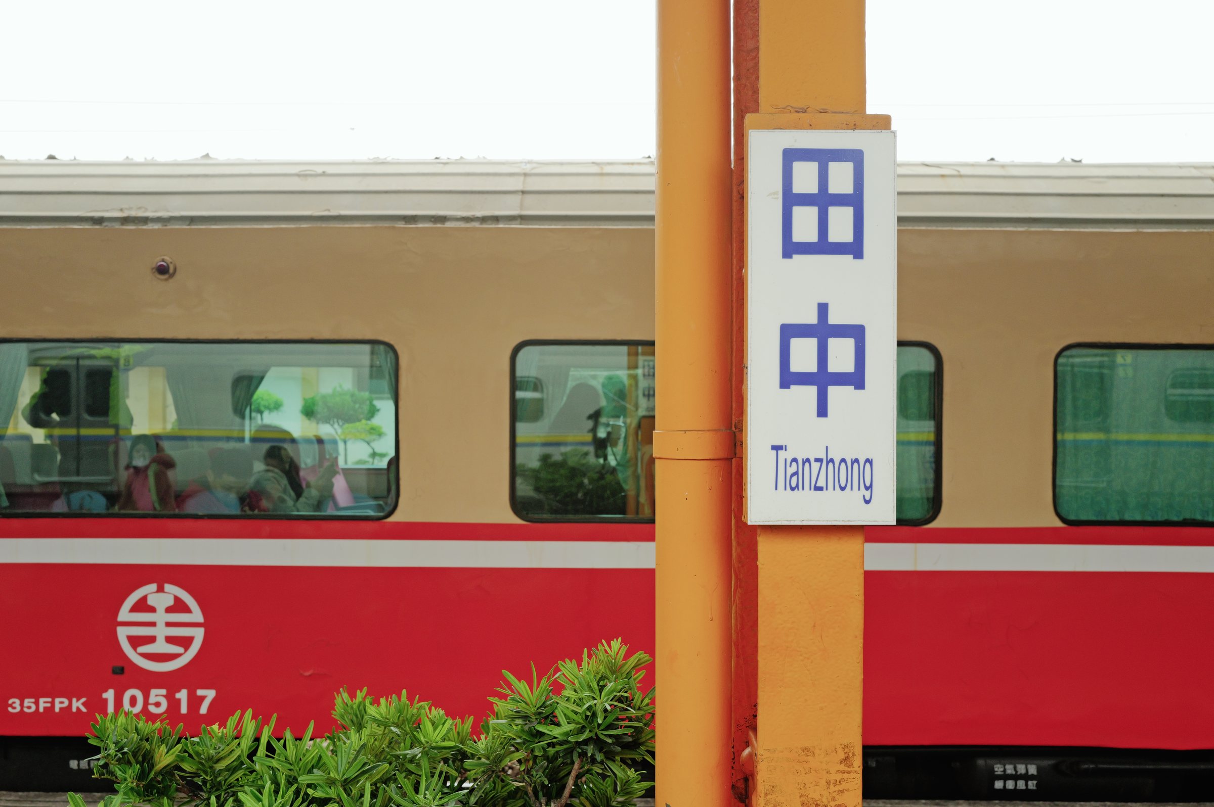 「田中」の駅名標と、その後ろに止まる赤い列車